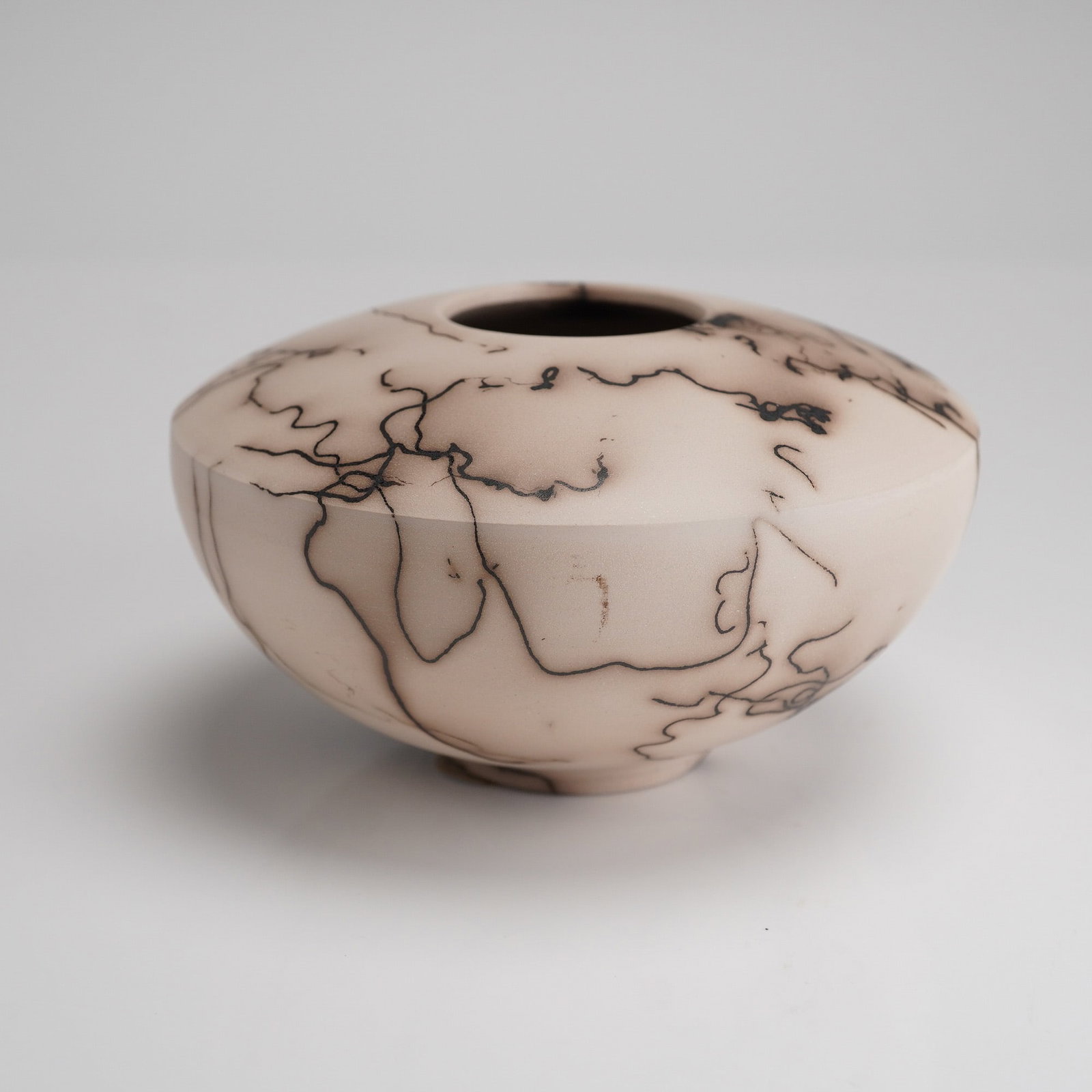 Contemporary Horsehair Raku Pottery Vessel: A contemporary ceramic vessel executed in the Horsehair Raku technique. The piece features a squat, compressed globular or seed pot form with a narrow, circular mouth opening. The body is composed of