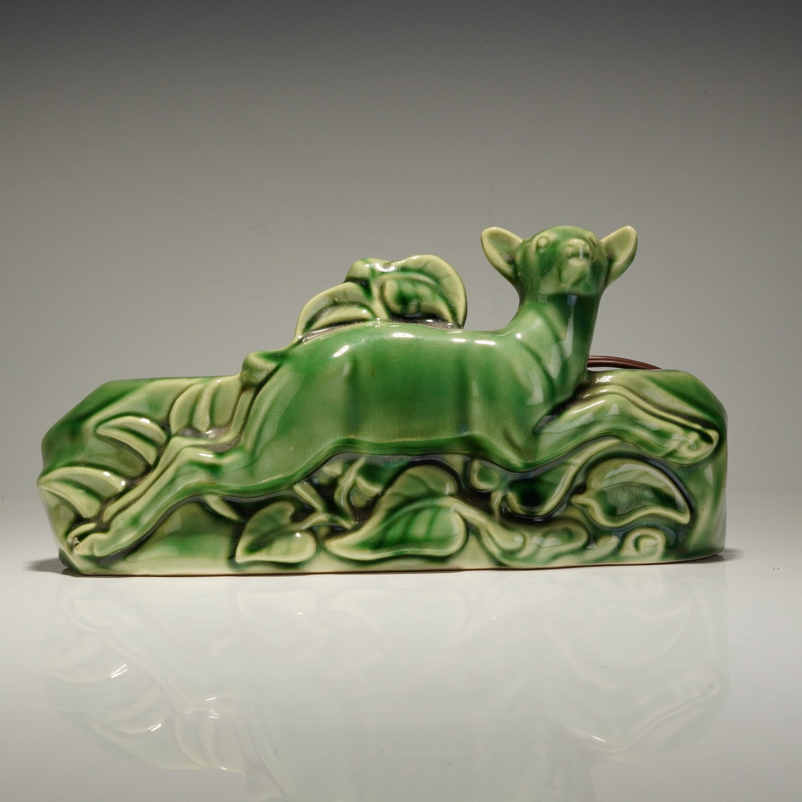 Mid-Century Modern Ceramic Green Glaze Deer TV Light and Planter: This mid-century modern ceramic green glaze deer TV light and planter features a stylized leaping deer set against a relief background of foliage. The piece is finished in a glossy green glaze. The re