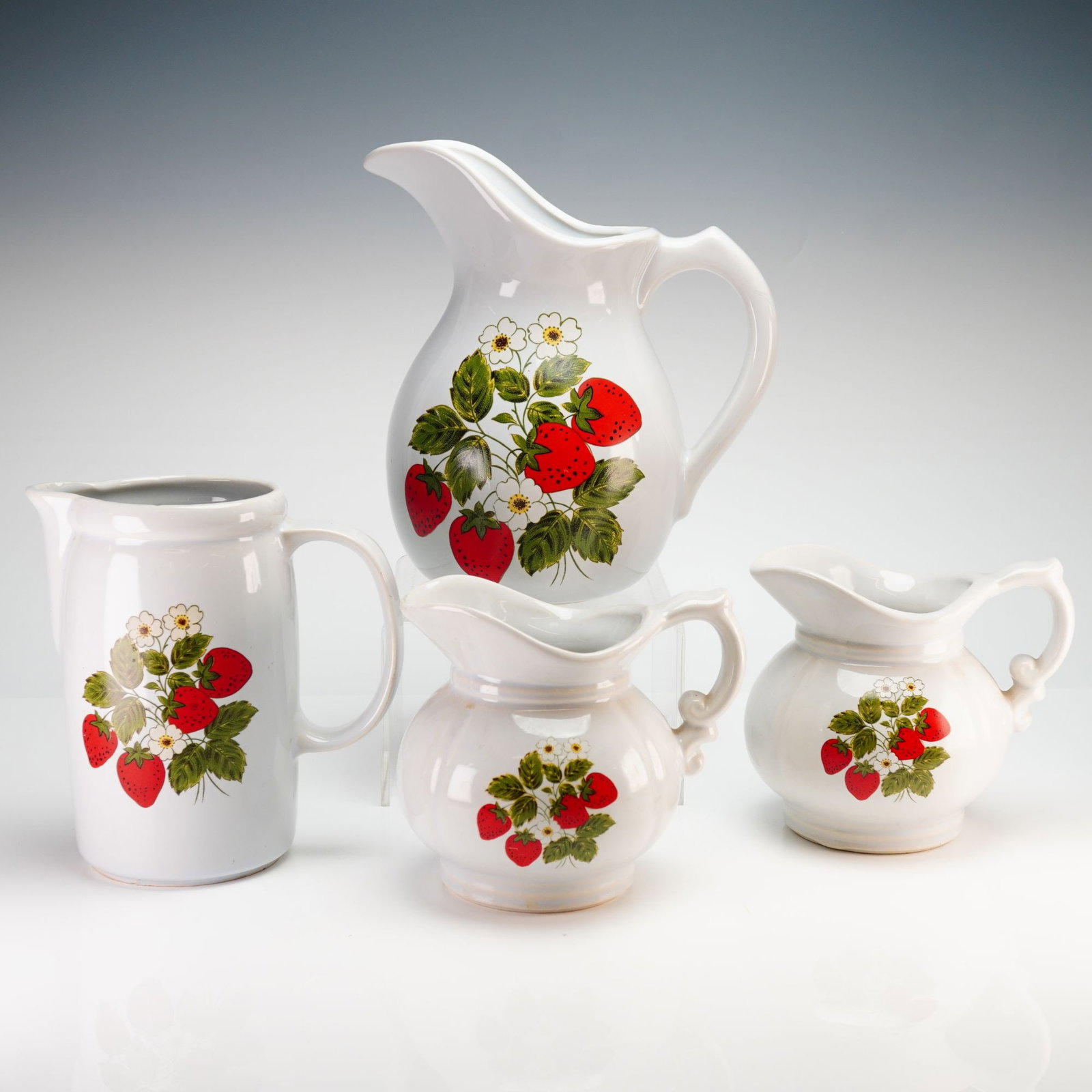4pc McCoy Strawberry Pitchers: A 4pc collection of McCoy strawberry pitchers and creamers. These vintage vessels are constructed from white-glazed earthenware and feature a colorful transfer pattern depicting clusters of ripe red s