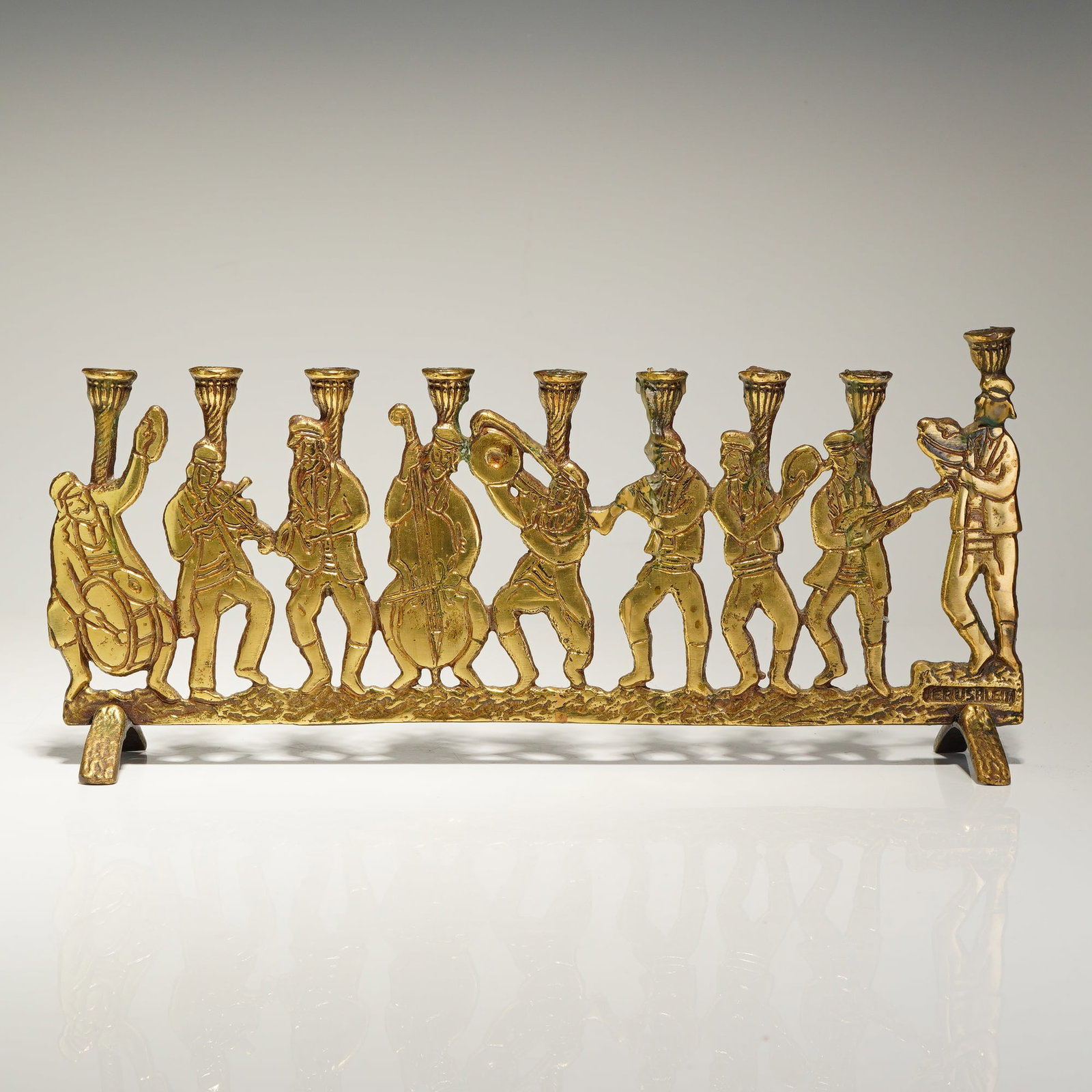 Judaica Jerusalem Klezmer Band Brass Hanukkah Menorah: A mid-century modern cast brass Hanukkah menorah depicting a Klezmer ensemble. The backplate features a horizontal relief of figures in traditional attire playing musical instruments, including a drum