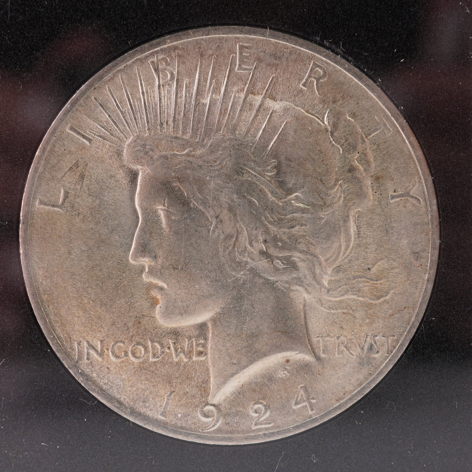 1924 Peace Silver Dollar: This 1924 Peace Silver Dollar is housed in a protective case. The obverse, designed by Anthony de Francisci, shows Liberty facing left wearing a radiate crown, with the inscriptions LIBERTY, IN GOD
