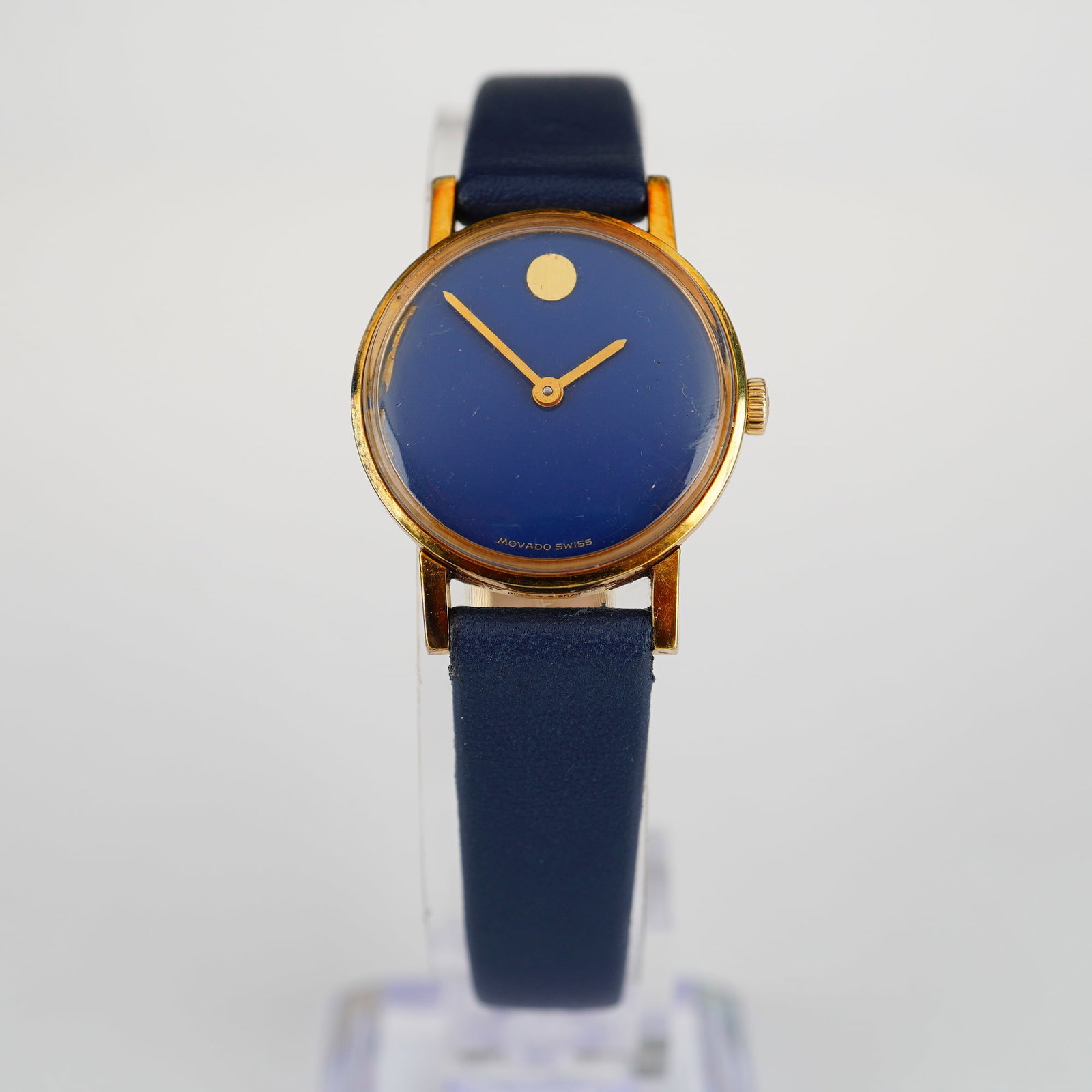 Movado Museum Watch: This Movado Museum wristwatch features a navy blue minimalist dial with a gold-tone concave dot at the 12 o'clock position and gold-tone dauphine hands. The dial is signed Movado Swiss at the 6 o'cloc