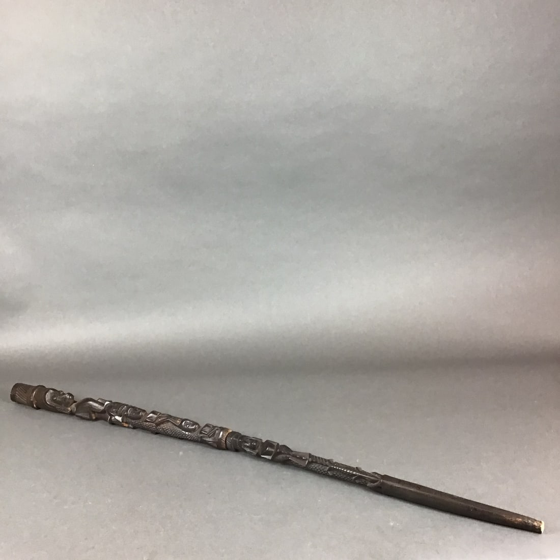 Northwest Coast Style Hand Carved Wooden Walking Stick Cane: This hand carved cane is fashioned from wood with a dark stained finish. The shaft features vertically stacked relief carvings in the Northwest Coast style, depicting stylized human and zoomorphic fig
