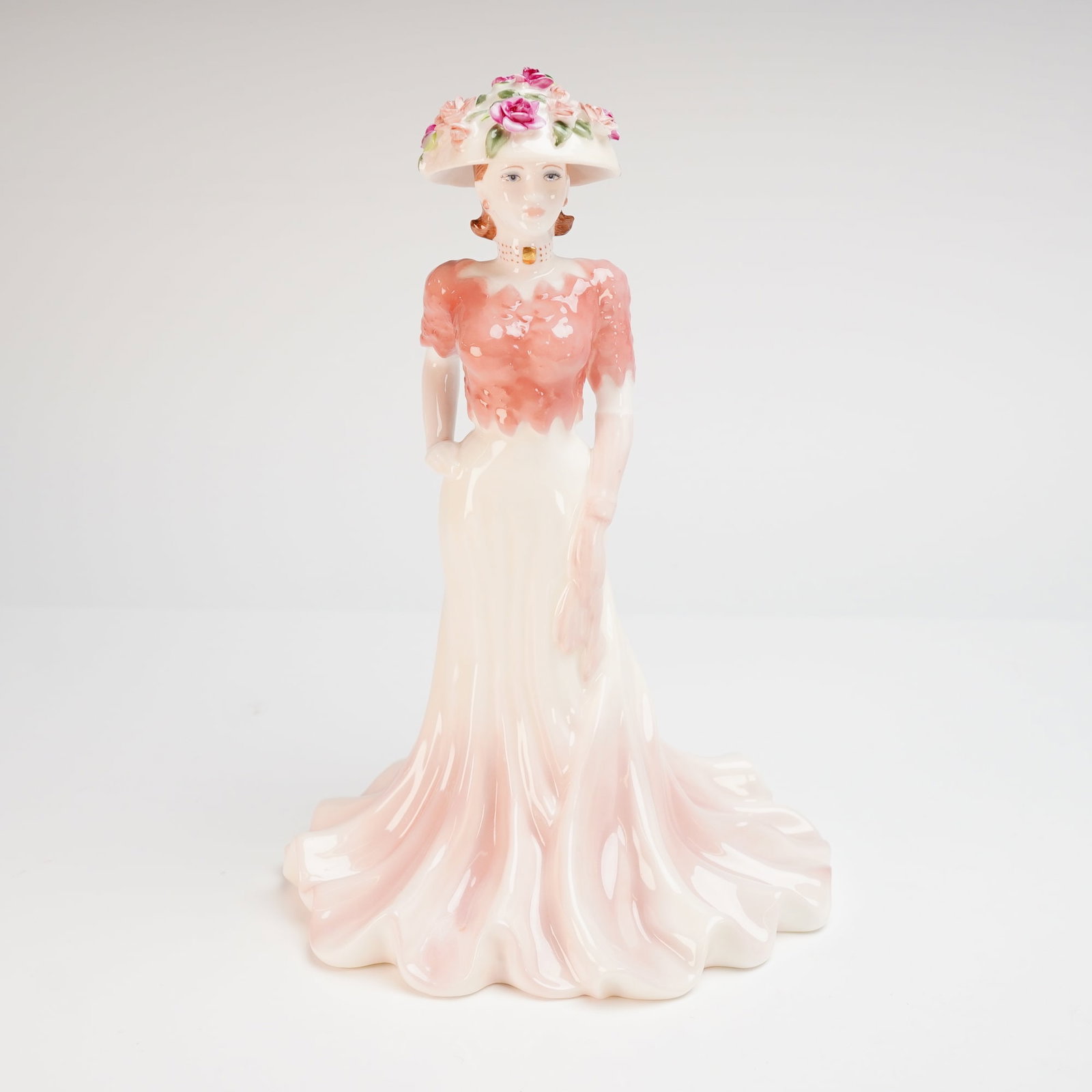 Coalport Bone China Ladies of Fashion Figurine Liz: A Coalport bone china figurine titled Liz from the Ladies of Fashion collection. The hand-decorated porcelain figure is depicted in a pale pink flowing gown with a textured rose-colored bodice and a f