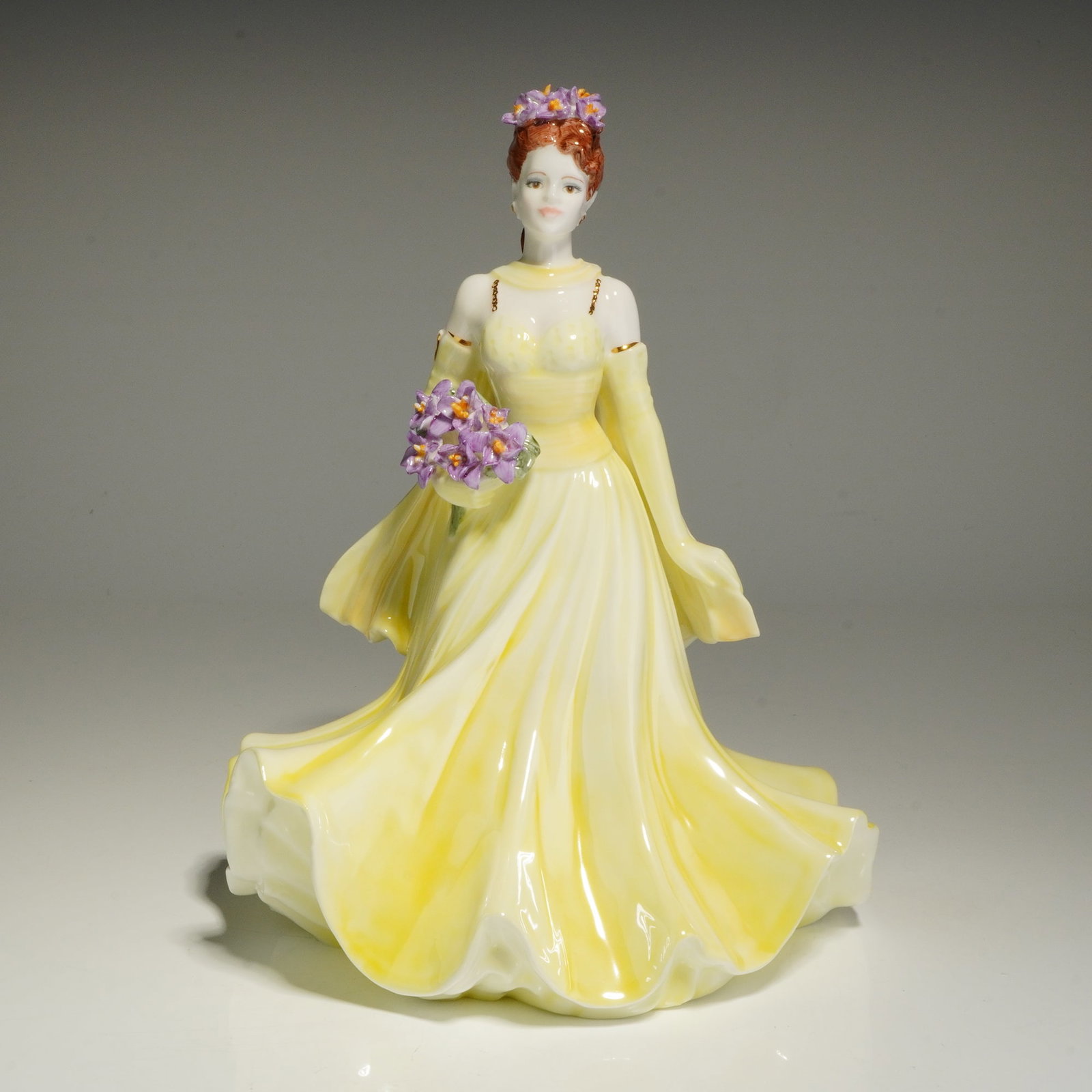 Coalport Bone China The Flower Ladies Collection Figurine, Dearest Iris: This hand-decorated figure depicts a woman with red hair wearing a pale yellow sleeveless gown and matching back stole. She is shown holding a bouquet of purple irises with a matching floral headpiece