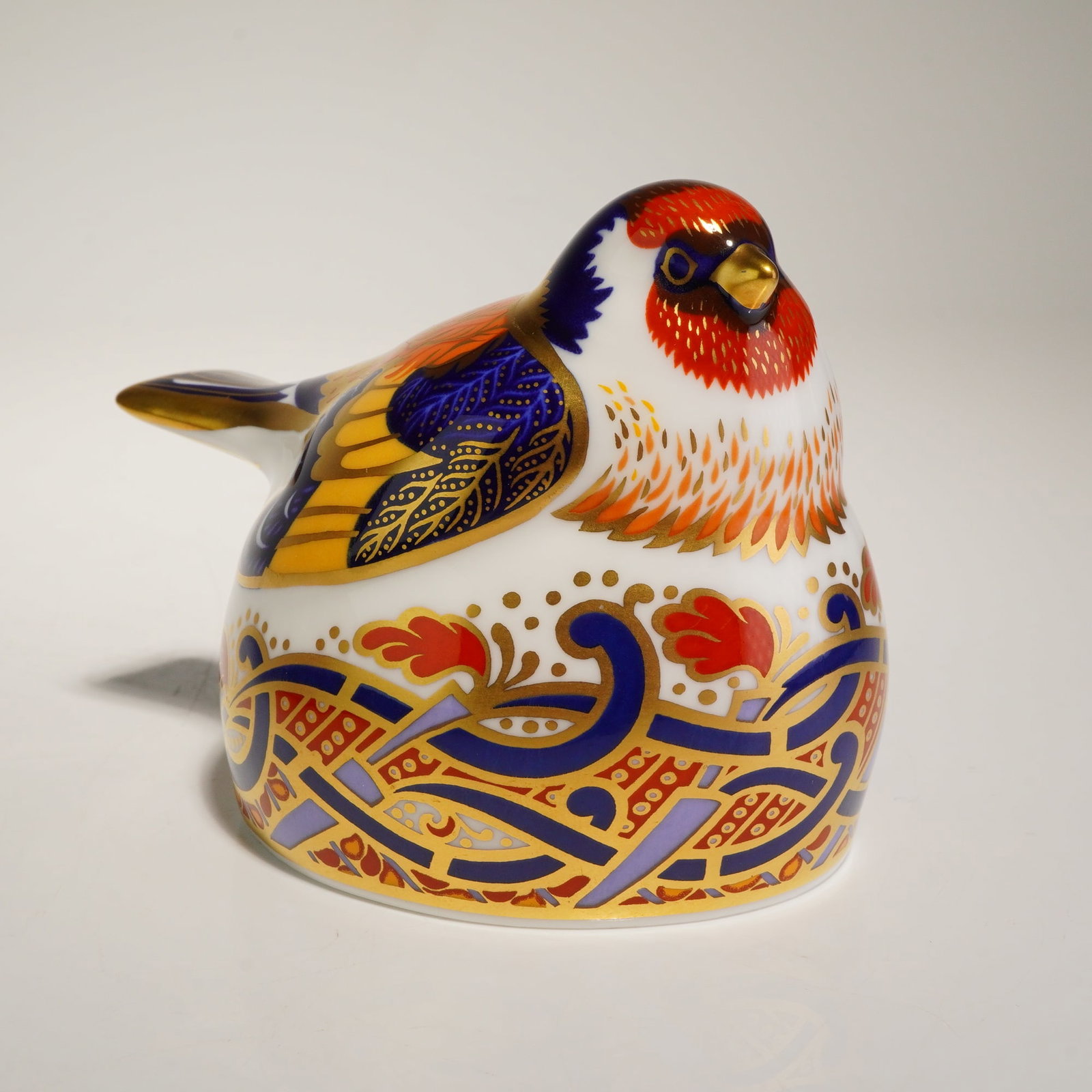 Royal Crown Derby Goldfinch Nesting Imari Bone China Paperweight: A Royal Crown Derby fine bone china paperweight titled Goldfinch Nesting. The figurine is modeled in a stylized avian form and decorated in an Imari-influenced palette of cobalt blue, iron-red, and or