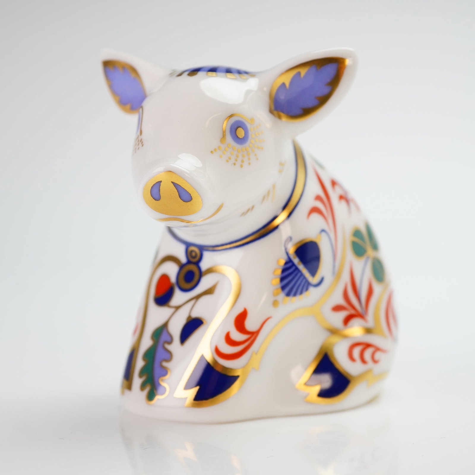 Royal Crown Derby Paperweight Sitting Piglet with Box: The piece features intricate polychrome decoration with floral and foliate motifs, including shamrocks and thistles, in shades of blue, red, green, and purple, heavily accented with gold gilding. The
