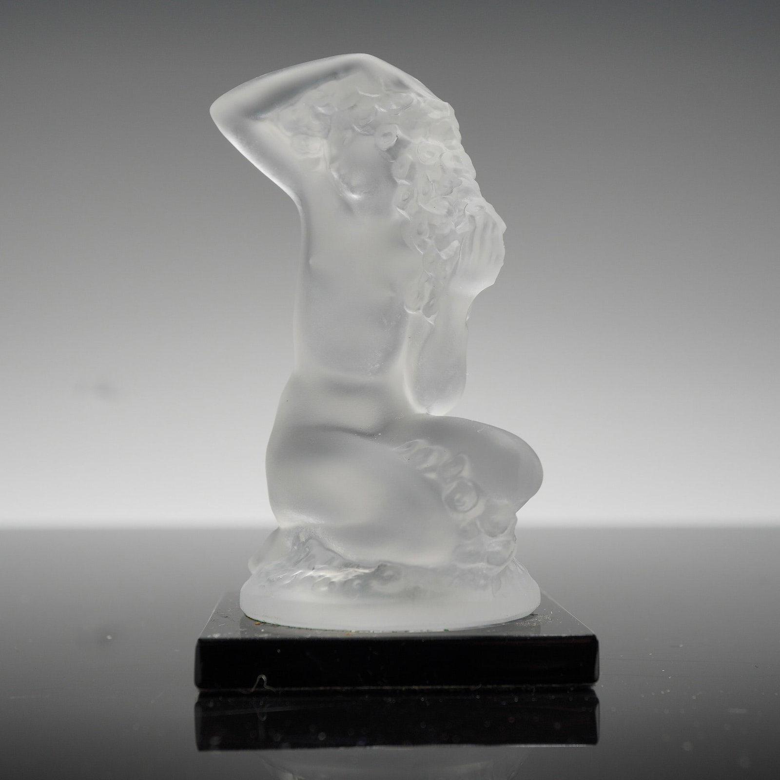 Lalique France Frosted Crystal Figurine, Floreal: The sculpture depicts a kneeling nude female figure with floral motifs in her hair, executed in frosted glass with a characteristic satin finish. The figure is mounted on a square black glass base. Th