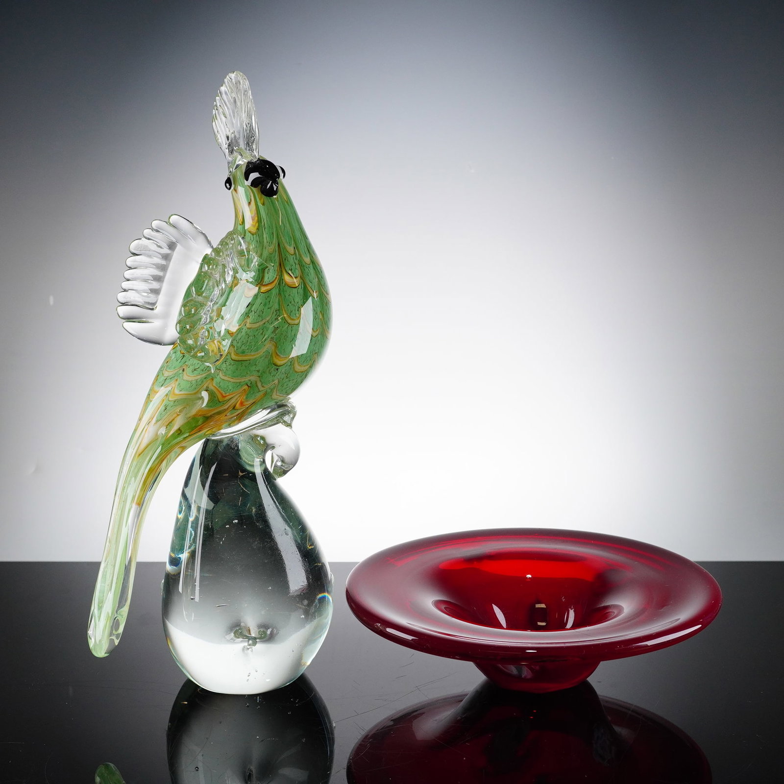 2pc Murano Hand-Blown Art Glass Cockatoo Figurine and Millefiori Bowl: Blown glass grouping includes a ruby red bowl with internal millefiori flowers and a hand-blown cockatoo bird figurine. The bird is expertly crafted with a green body featuring internal combed yellow
