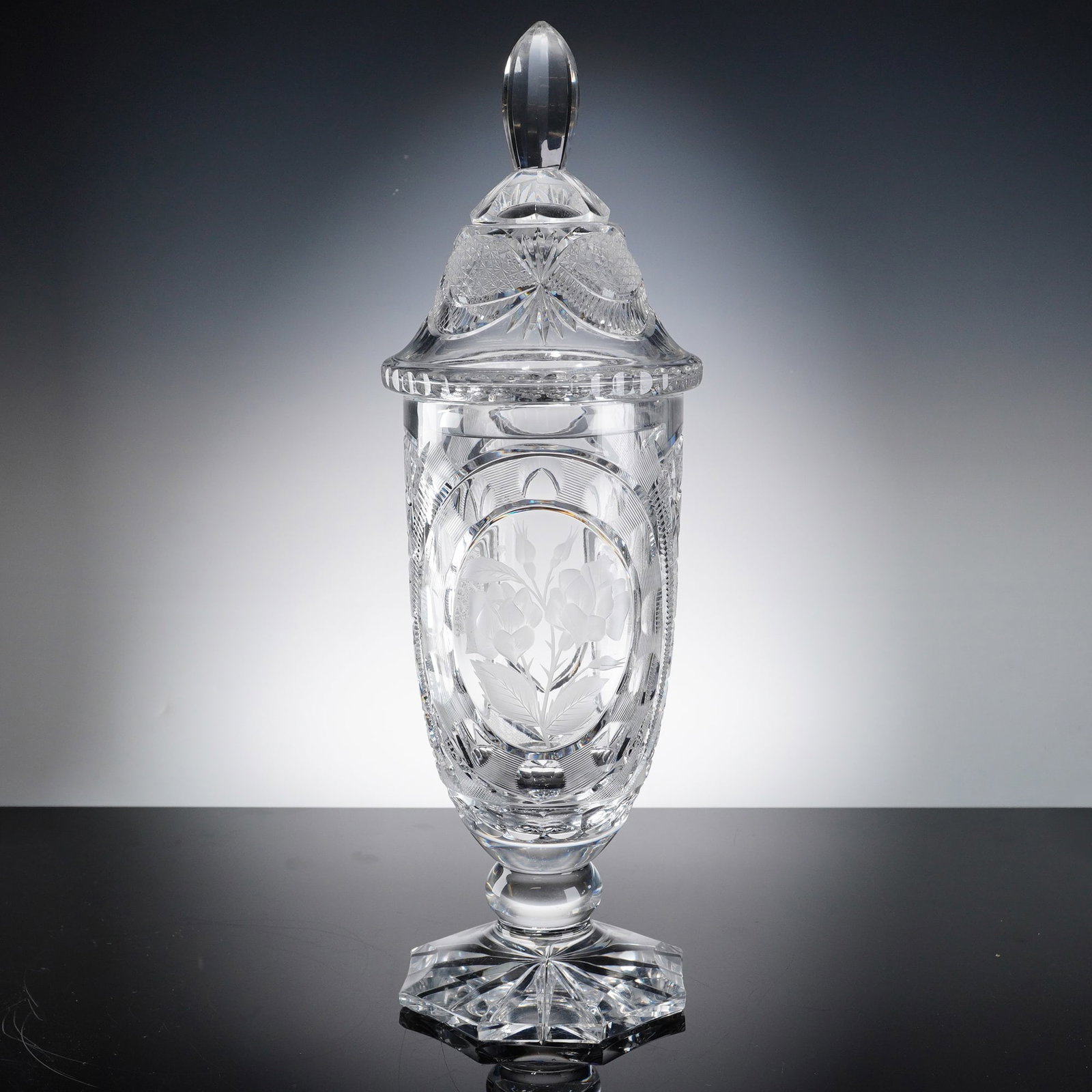 Bohemian Intaglio Cut and Etched Lead Crystal Lidded Urn: This lidded crystal vase is a premier example of Bohemian glasswork, characterized by its intricate floral etchings and complex geometric cutting. The cylindrical body features four large oval medalli