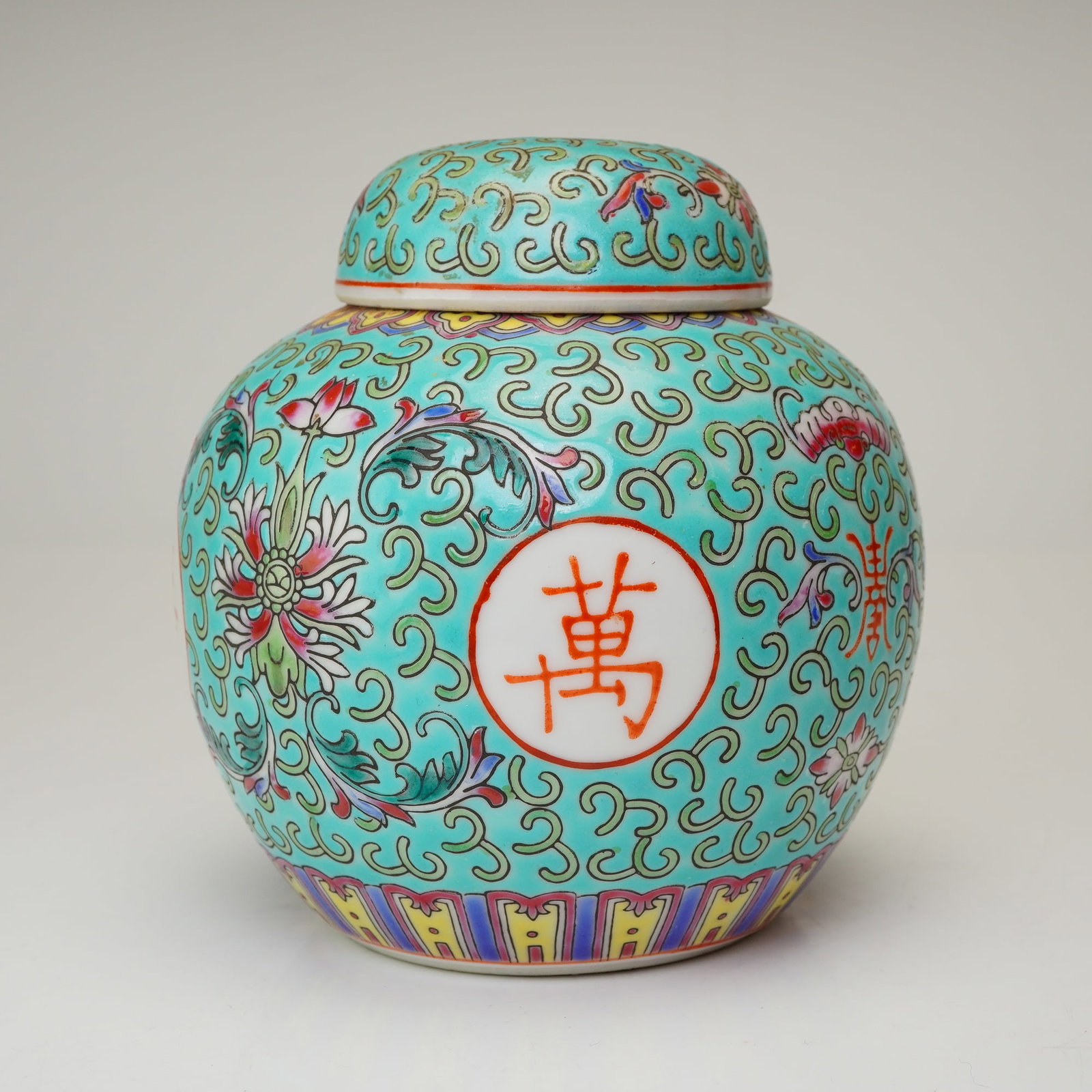 Chinese Turquoise Lidded Ginger Jar: The exterior features a vibrant turquoise ground embellished with a pattern of scrolling tendrils. Four circular medallions contain iron-red characters. These medallions are interspersed with stylized
