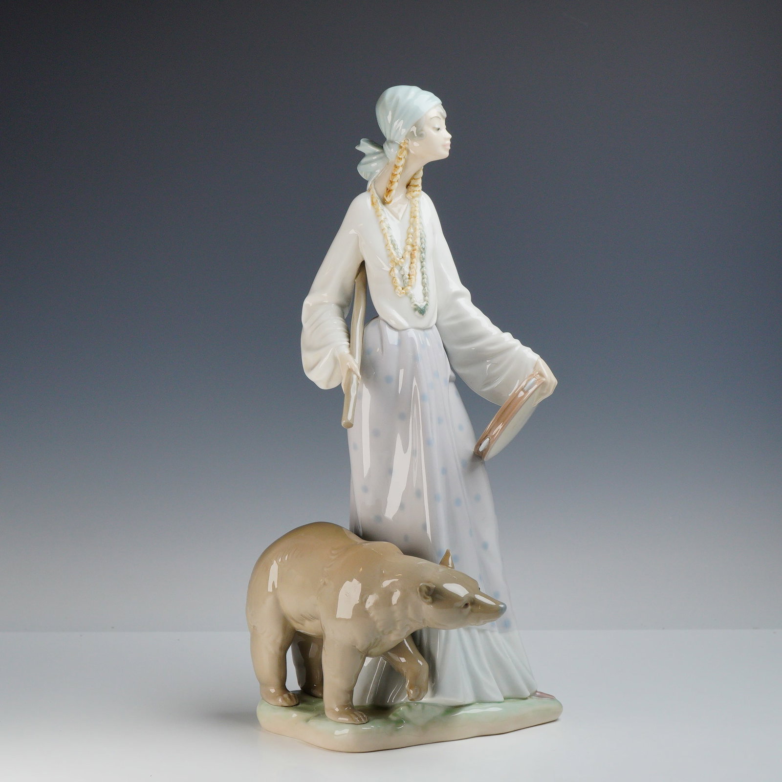Lladro Gypsy Woman with Bear Porcelain Statue, Model 4919: This glazed Lladro porcelain statue is titled Gypsy with Bear, model number 4919. Designed by sculptor Salvador Debon, the piece depicts a standing woman in traditional attire. She wears a long, pale-