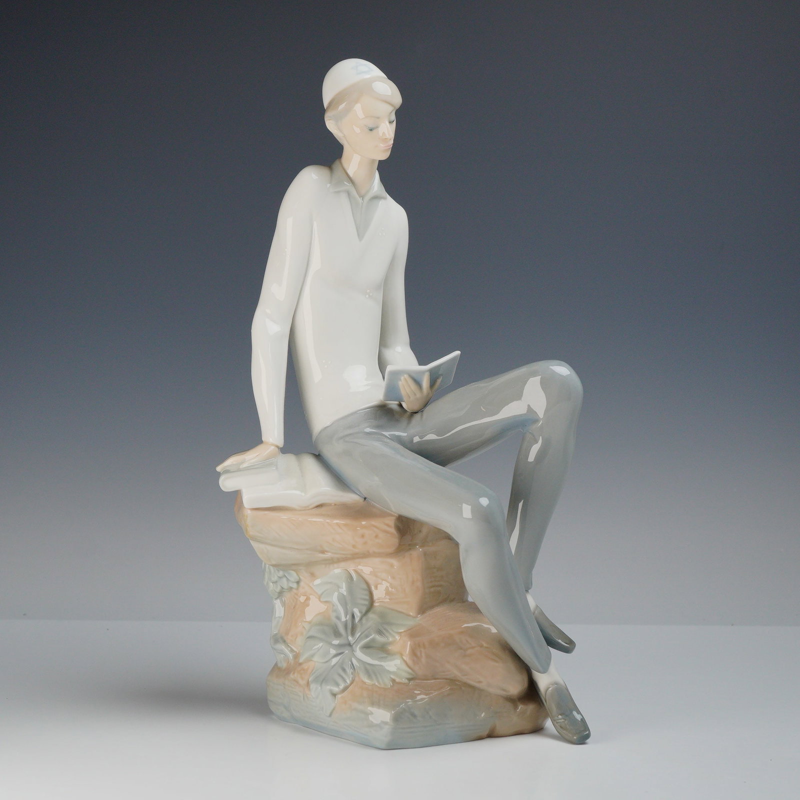 Lladro Porcelain Figurine Hebrew Student 01004684: A glazed porcelain figurine manufactured by Lladro, model number 5245, titled The Reader or El Lector and commonly identified as the Hebrew Student. The figurine depicts a slender young man in a conte