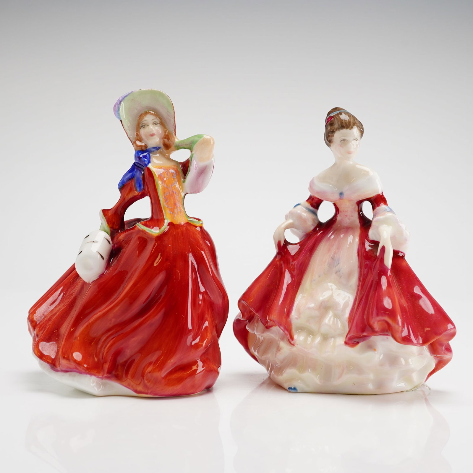 2pc Royal Doulton Figurines, Autumn Breezes HN2176 & Southern Belle HN3174: These mini hand-decorated glazed bone china figures feature vibrant red color palettes and a high-gloss finish. Autumn Breezes, designed by Leslie Harradine with a 1939 copyright, depicts a woman in a