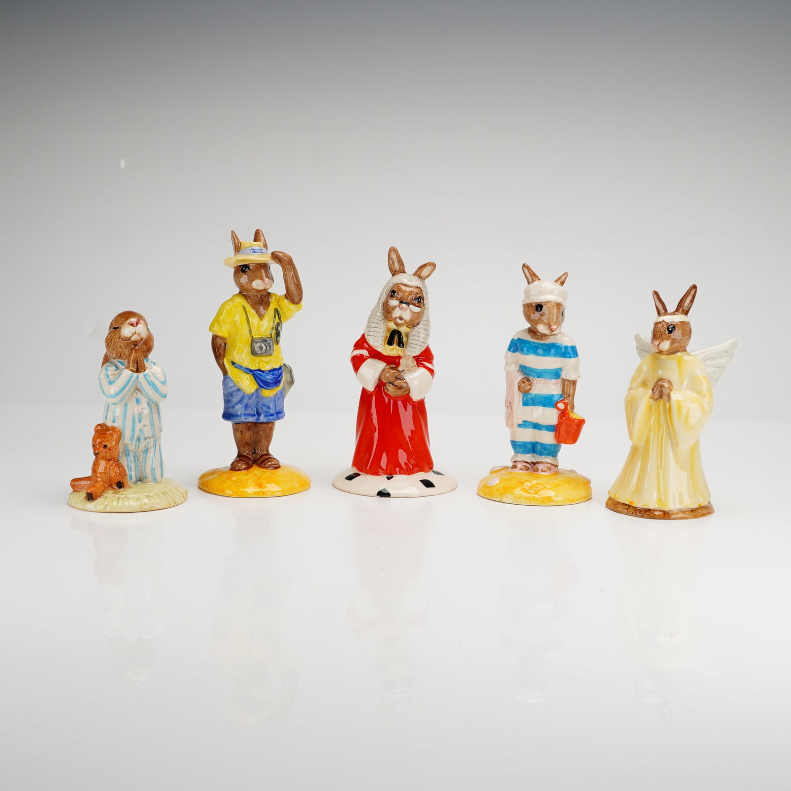 5pc Royal Doulton Bunnykins Figurines: A collection of five Royal Doulton glazed ceramic Bunnykins figurines featuring various anthropomorphic rabbit characters. The group includes Bedtime Bunnykins (DB55) in striped pajamas with a teddy b