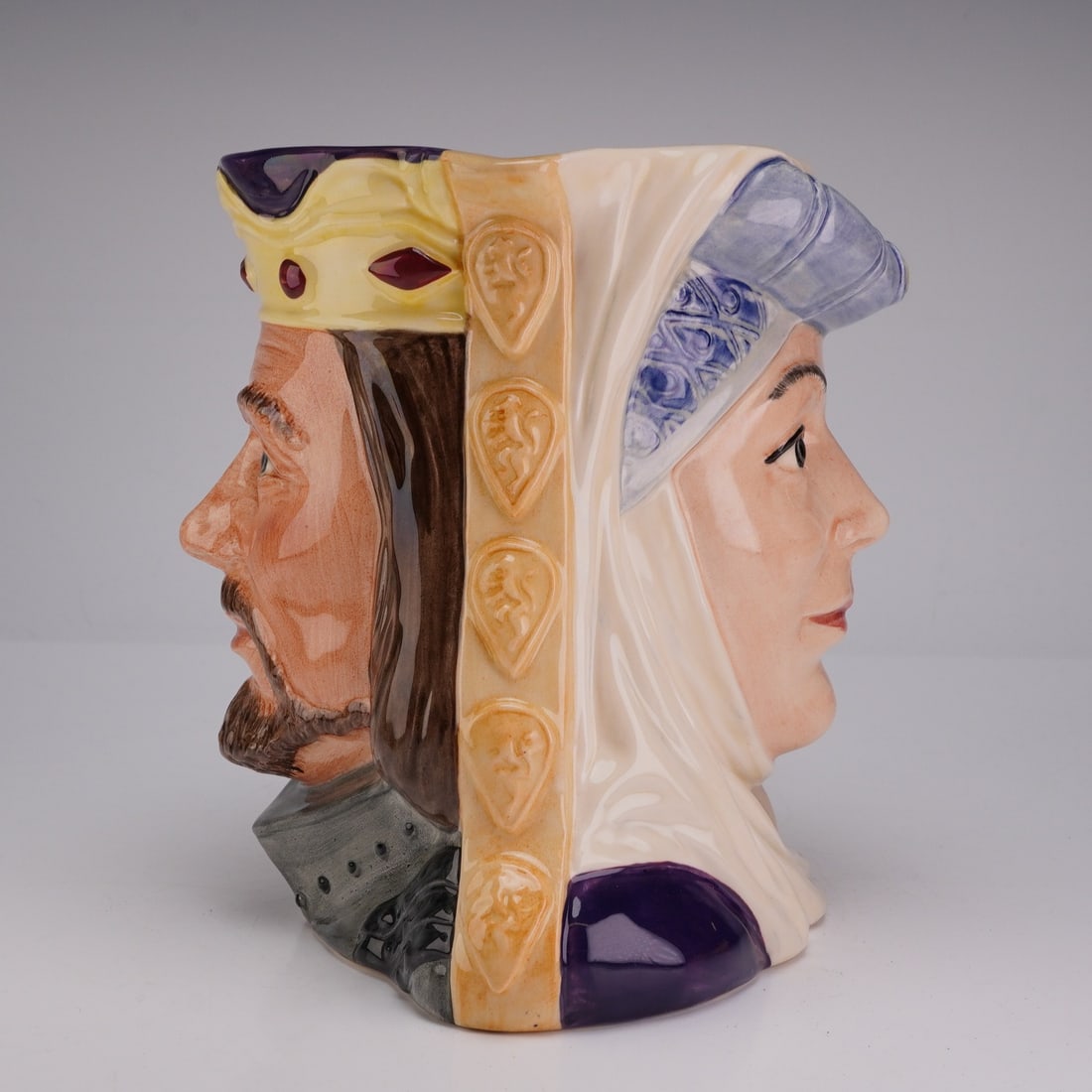 Royal Doulton Star-Crossed Lovers Double-Face Character Jug, King Arthur & Guinevere D6836: This double-sided vessel features two faces, with Guinevere on one side depicted in a white wimple and blue-jeweled headdress, and King Arthur on the reverse shown in gray armor and a gold crown set w
