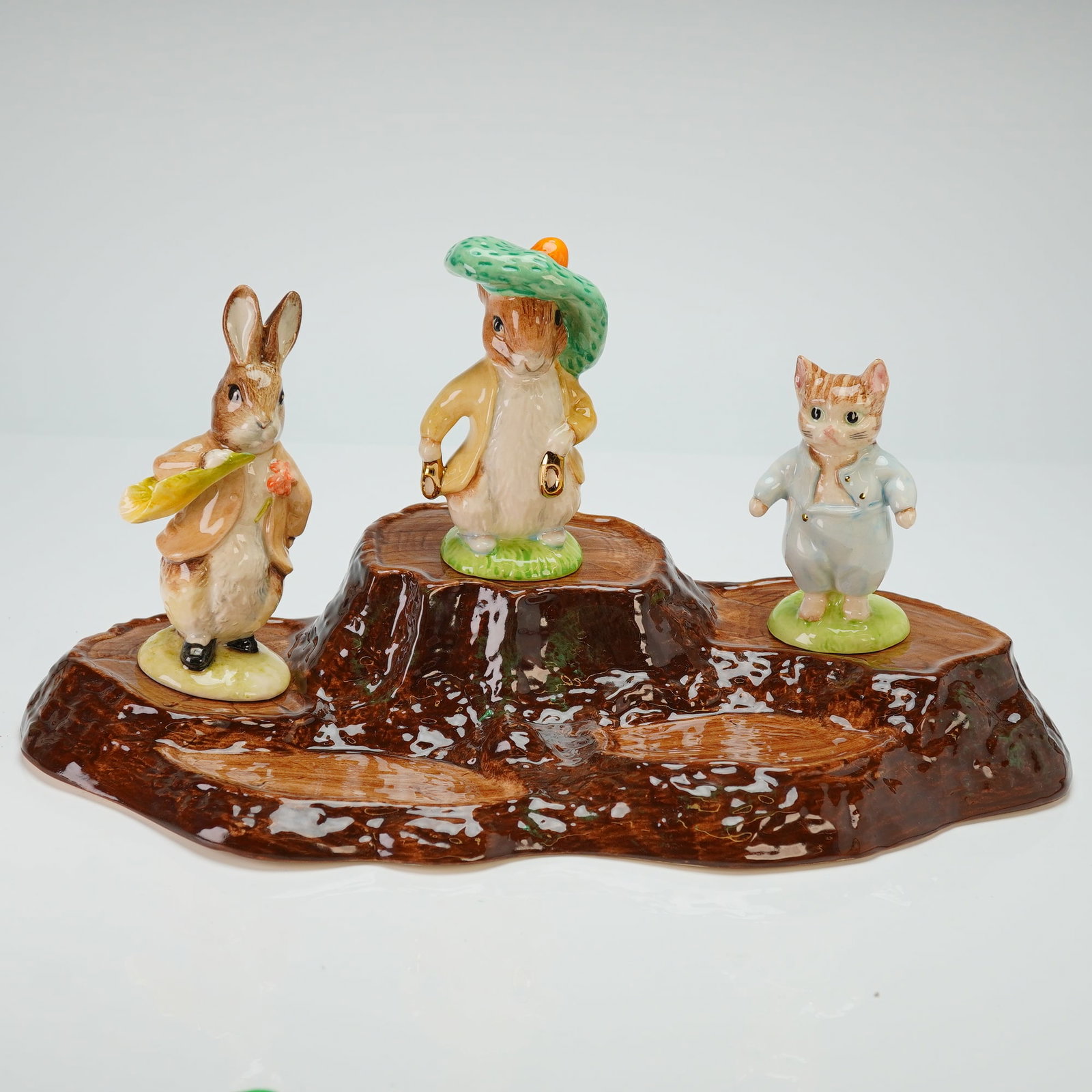 4pc Beswick Beatrix Potter Tree Stump Base and Three Figurines: The collection consists of a large ceramic display base molded and glazed to resemble a tree stump, along with three individual figurines including Tom Kitten, Benjamin Bunny in a green tam-o-shanter,