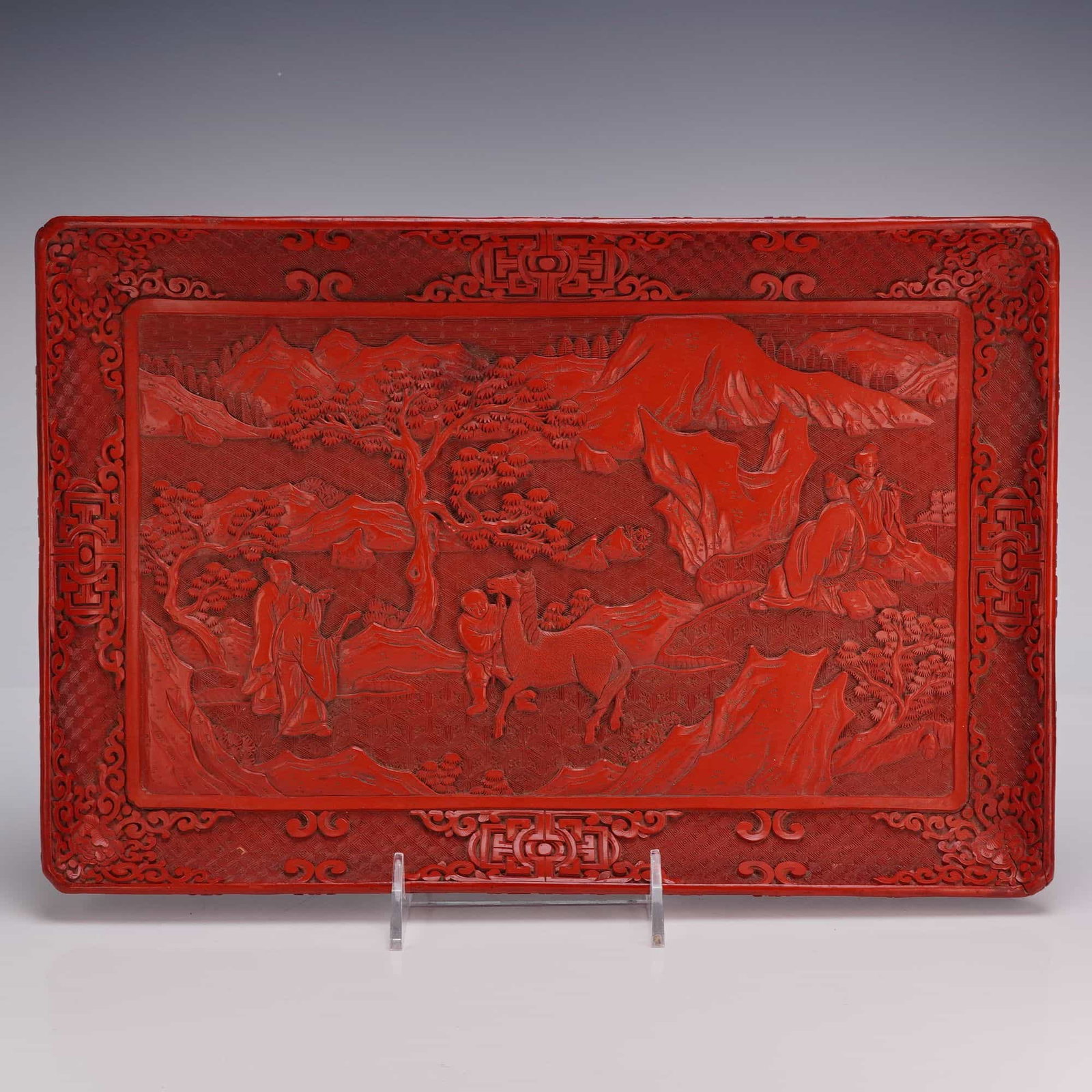 Chinese Cinnabar Lacquer Rectangular Form Tray, Figures in Landscape: A rectangular Chinese cinnabar lacquer tray carved with a key pattern and a scroll and floral border around the rim, featuring a central scene of figures and horses in a landscape. Dimensions14"L x 9.