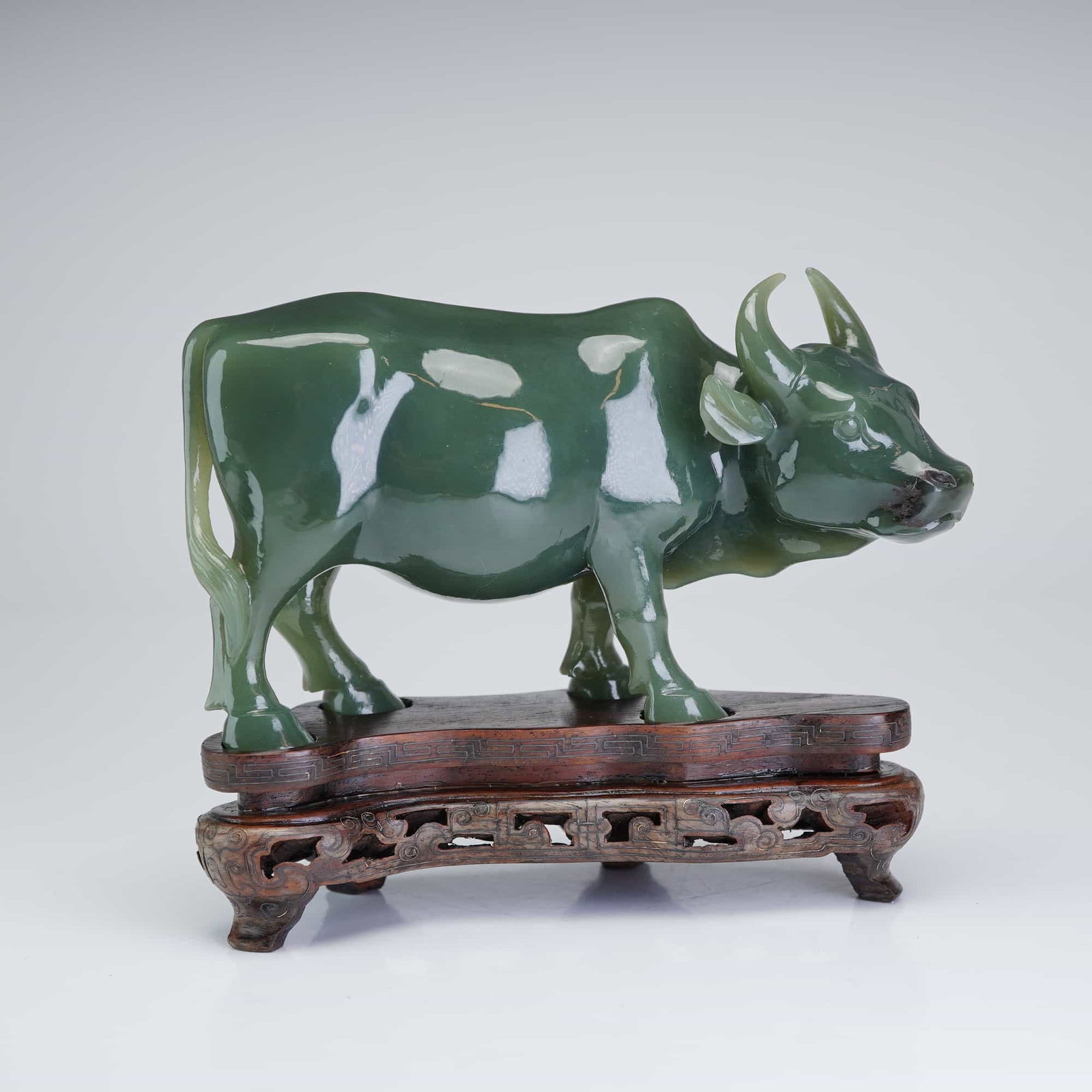 Chinese Carved Spinach Jade Water Buffalo Figure: The stone exhibits characteristic natural dark inclusions, particularly visible on the muzzle, and lighter cloud-like veining across the flanks. The water buffalo is naturalistically modeled in the ro