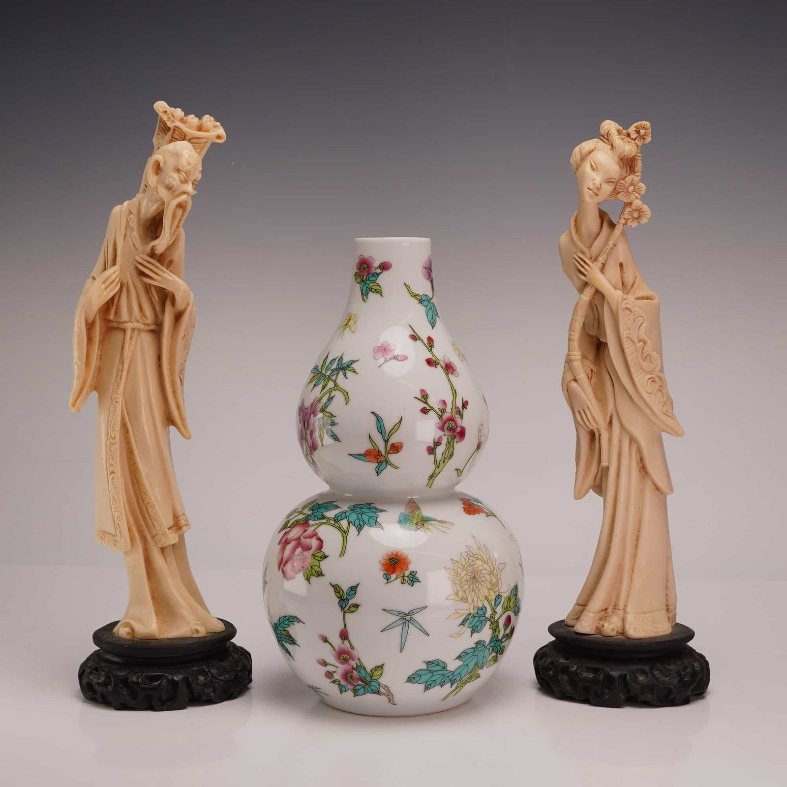 A Chinese Famille Rose Porcelain Double Gourd Vase and a Pair of Resin Figurines: This three-piece group of decorative arts includes a porcelain vase and a pair of resin figurines. The porcelain vase is of double gourd or hulu form, featuring a white glaze decorated in a famille ro