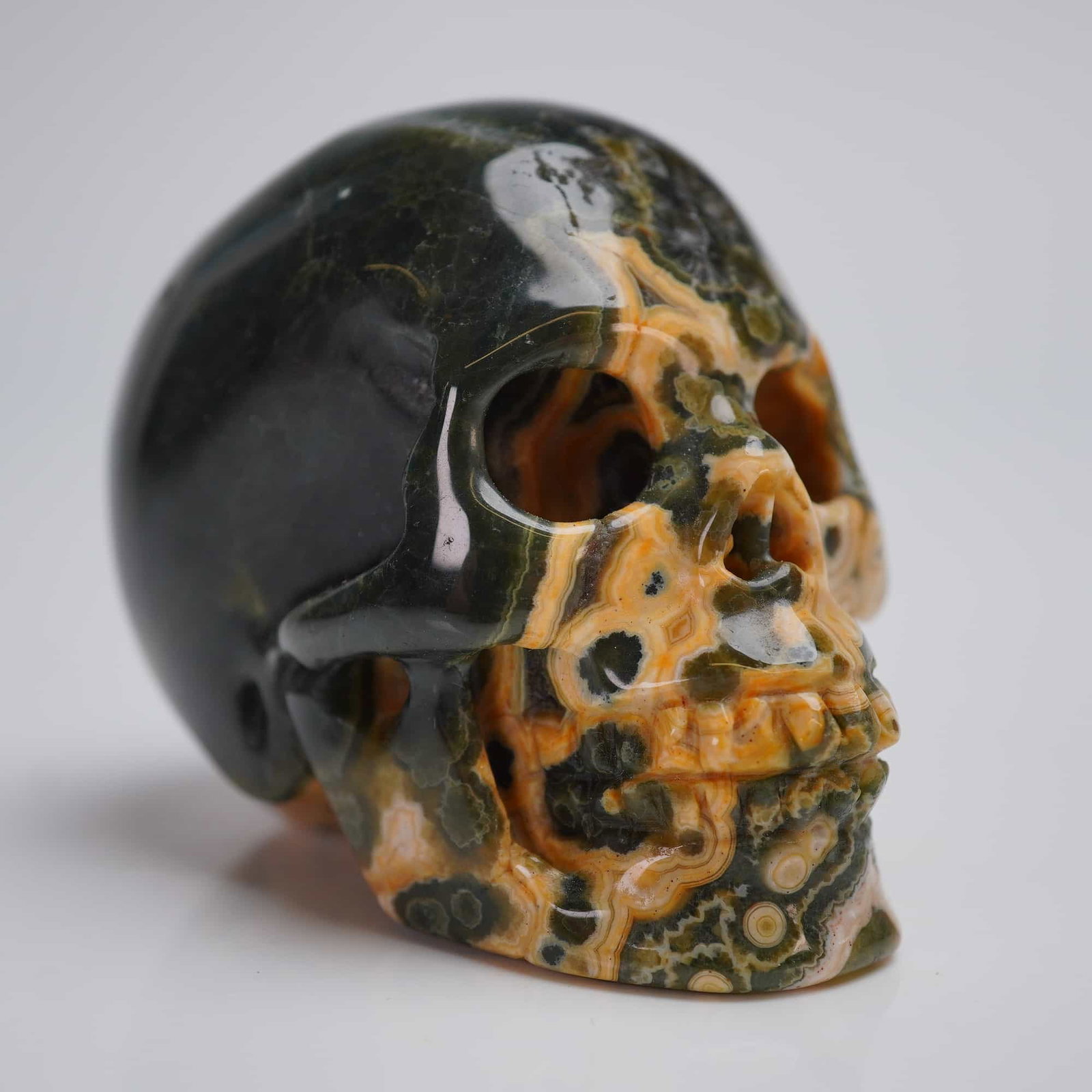 Ocean Jasper Crystal Hand Carved Skull: A contemporary lapidary sculpture depicting a stylized human skull. The piece is hand carved from highly polished Orbicular Jasper, commonly marketed as Ocean Jasper or Carved Kambaba Jasper. The ston