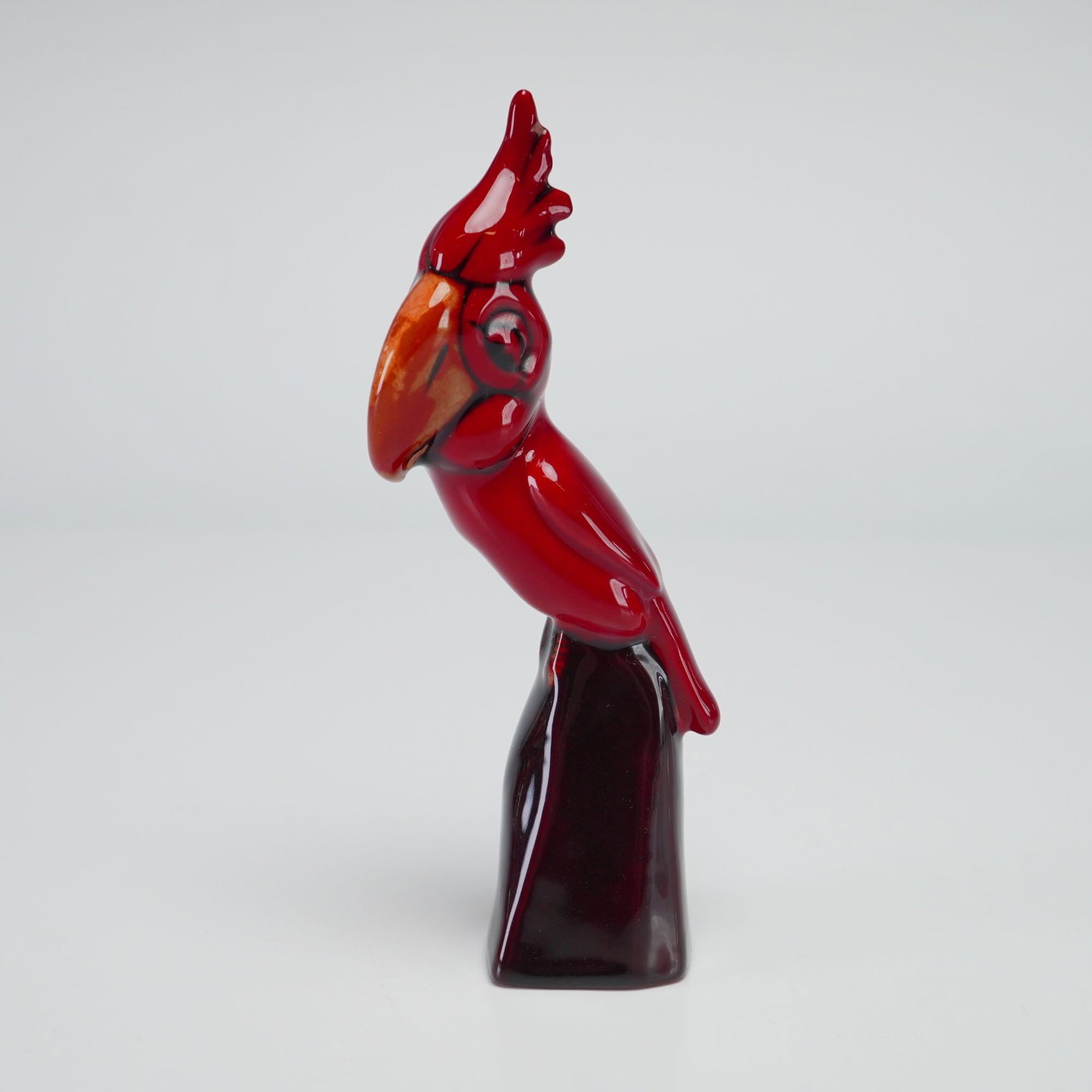Royal Doulton Experimental Flambe Figurine, Character Parrot on Pillar HN884: Depicts a bird on base, specifically a cockatoo with a prominent crest and a large, curved beak. The bird is perched on a pillar form. The piece is made of porcelain and finished in the signature Roya