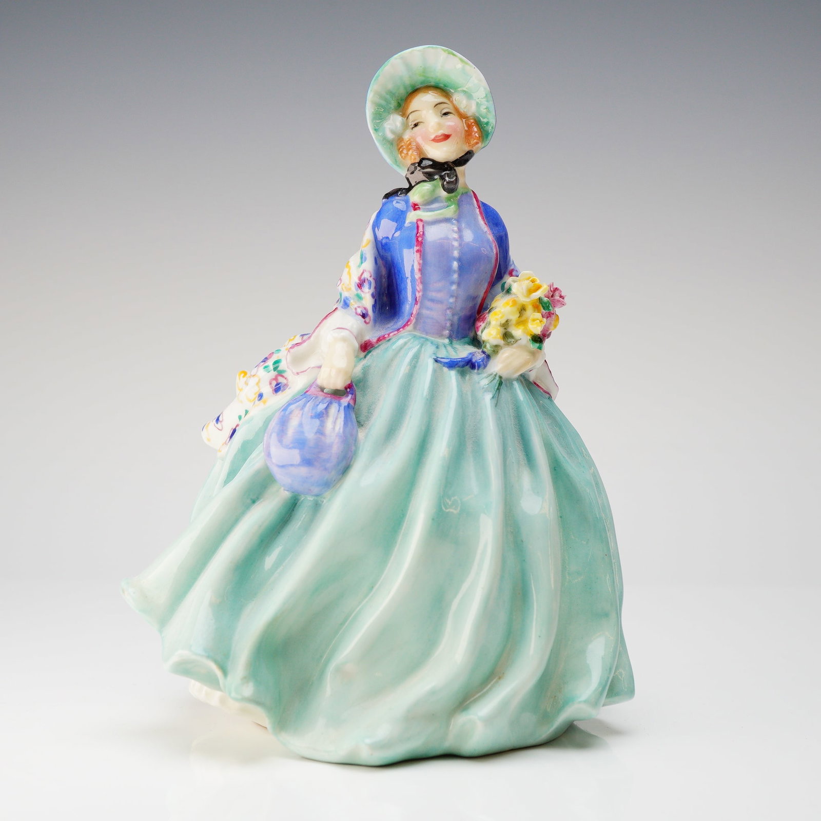 Royal Doulton Honey Bone China Figurine HN 1910: A single Royal Doulton Honey HN1910 bone china figurine, glazed and hand-painted. The figurine depicts a woman in a sweeping, mid-20th-century stylized period dress, featuring a voluminous aqua-green