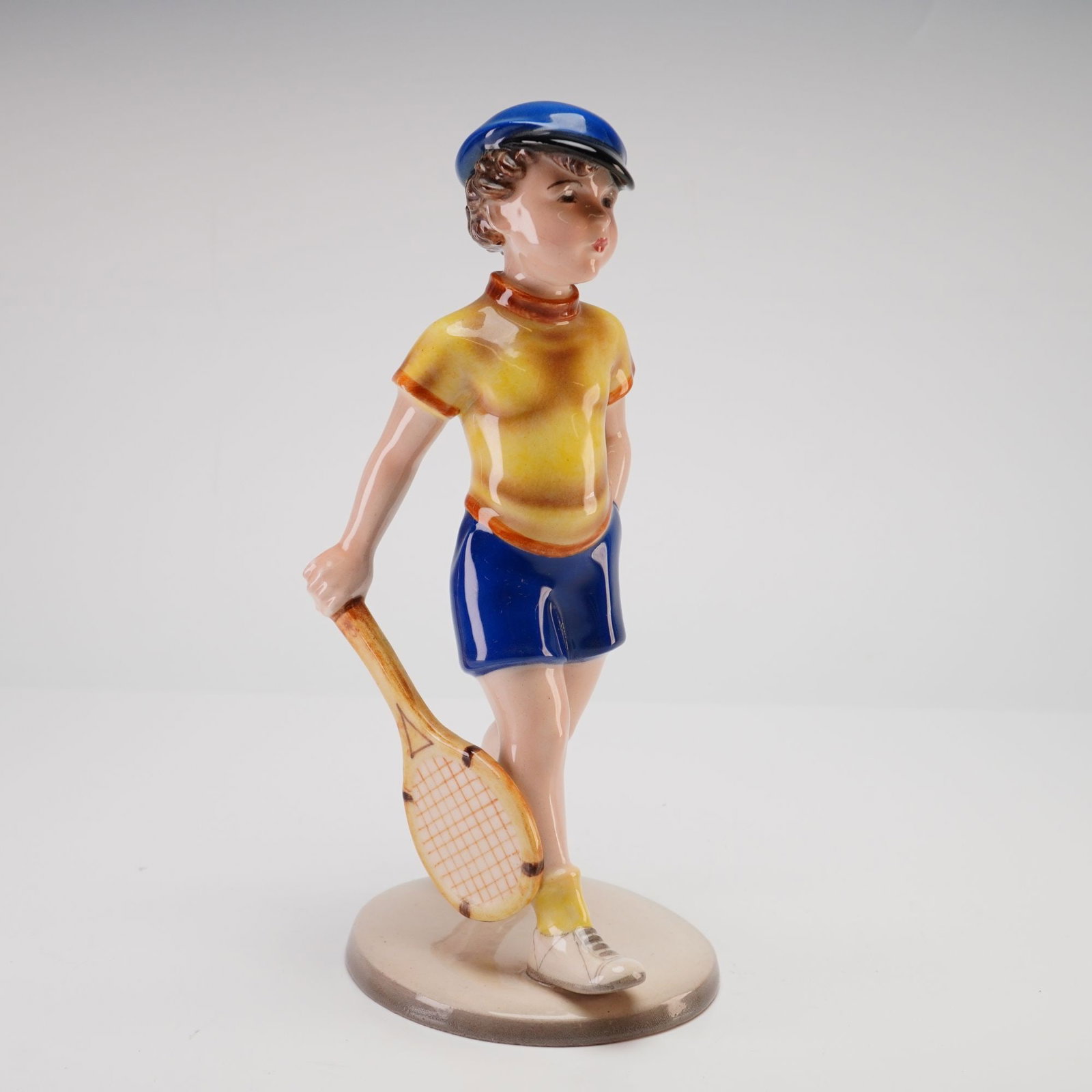 Keramos Wien Knight by Stephan Dakon Ceramic Figurine, Tennis Player Model Number 2000: Vienna hand-painted figure designed by Austrian artist Stefan Dakon (1904-1992), known for his contributions to Art Deco sculpture. This example, numbered 5 of 8, portrays a young boy dressed in a yel