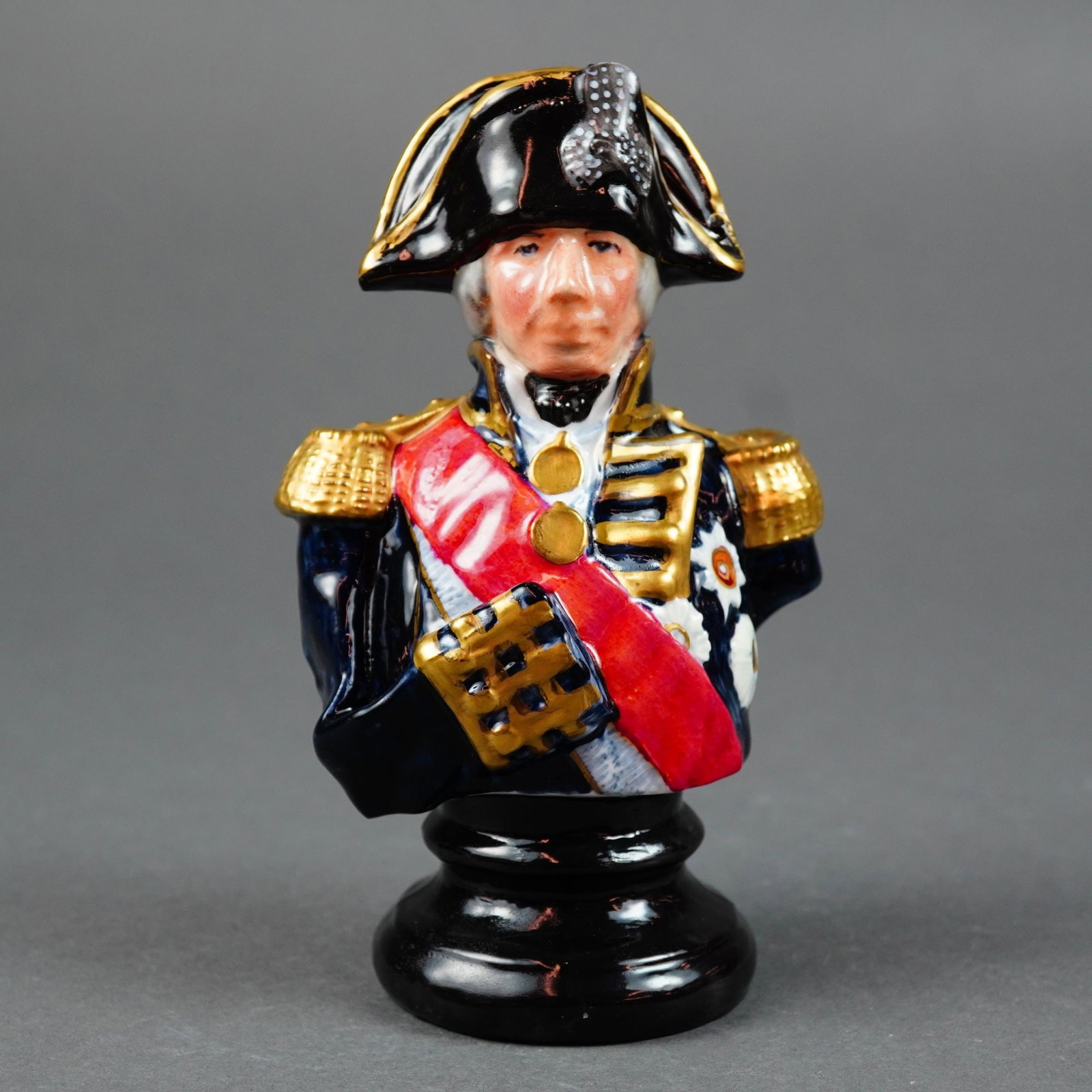 Michael Sutty Admiral Nelson Porcelain Bust: This hand-painted porcelain bust by Michael Sutty for The Porcelain Manufactory, England, depicts Admiral Lord Nelson in his naval uniform. The figure is finely detailed with a black bicorne hat featu