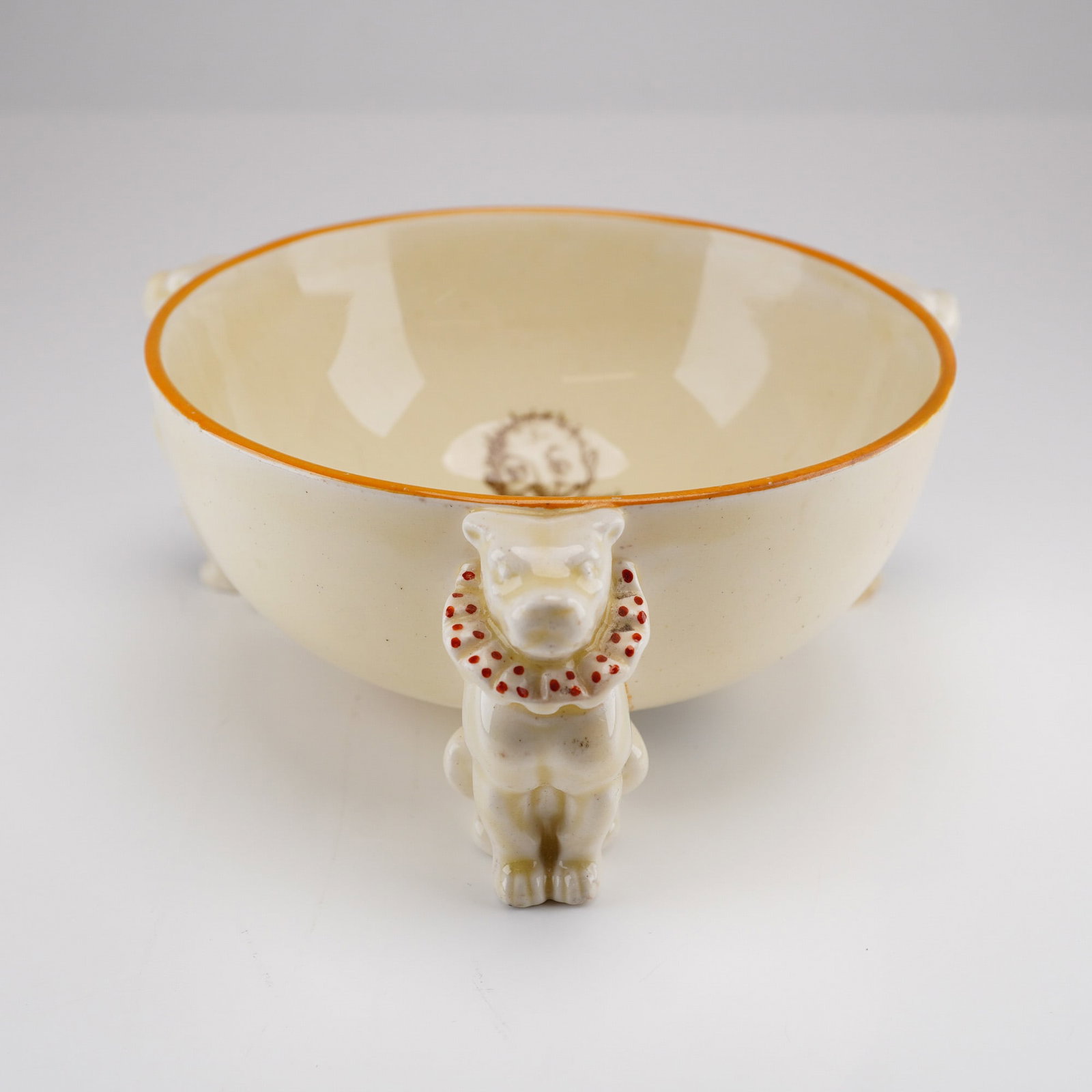 Wedgwood Creamware Mr. Punch Small Footed Bowl with Figural Dog Supports Circa 1898: This is a fine late 19th-century Wedgwood creamware footed bowl, dated circa 1898. The vessel features a creamy-white glazed body finished with a hand-painted orange rim. The bowl is supported by thre