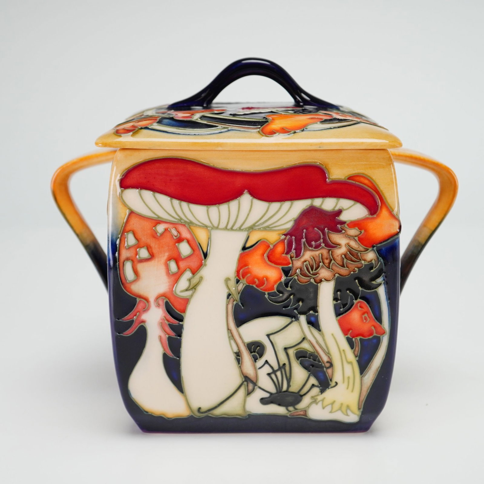 Moorcroft Pottery by Emma Bossons Lidded Biscuit Barrel, Toadstool Carnival: A 2009 limited edition 159 out of 200, the jar is constructed of fine earthenware with a square body, two integral side handles, and a coordinating lid featuring a central loop handle. The decoration
