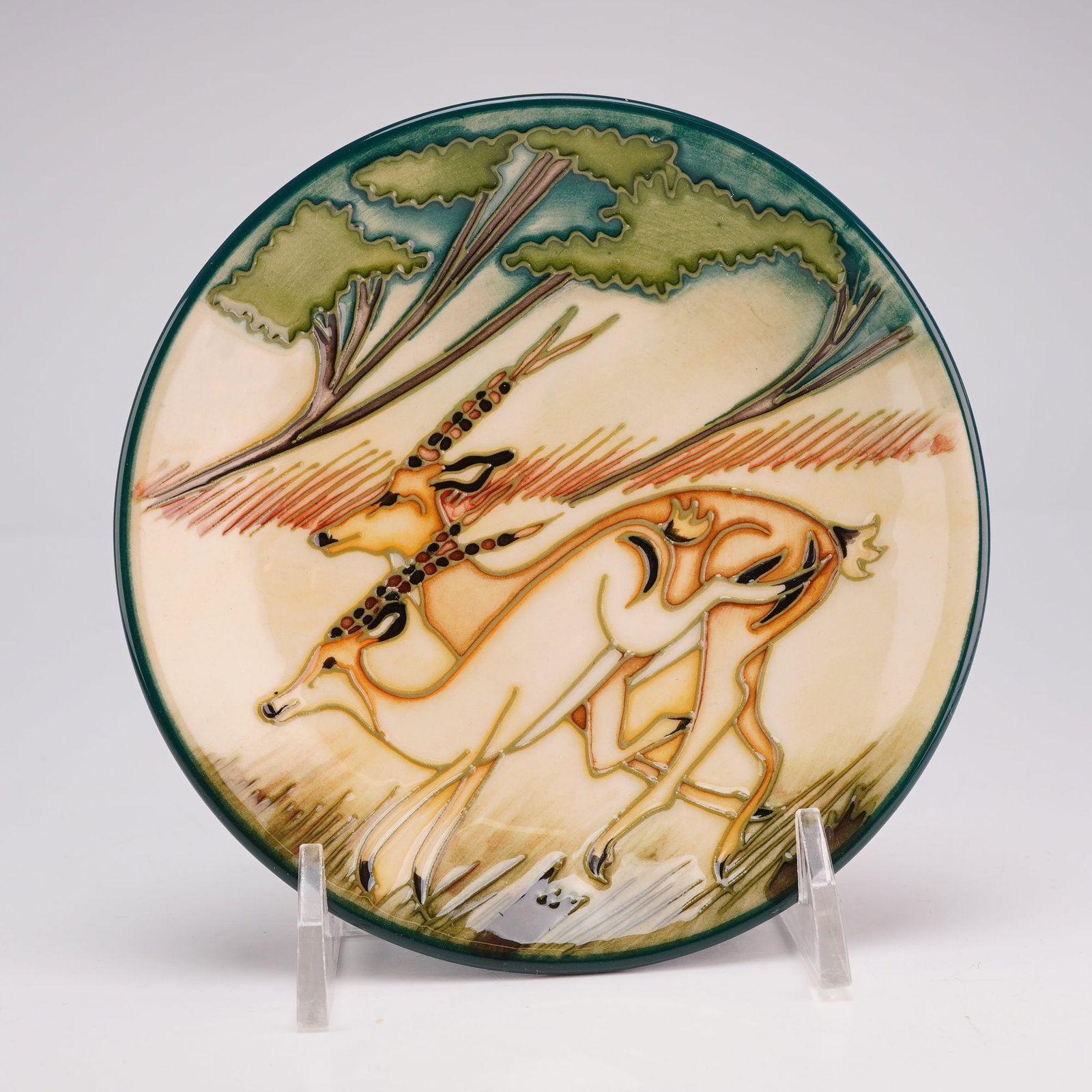 Moorcroft Pottery by Kerri Goodwin Pin Dish, Impala: This circular earthenware dish features hand-painted tube-lined decoration under a clear glaze. The design depicts two impalas in profile running through a landscape with stylized umbrella-topped tree