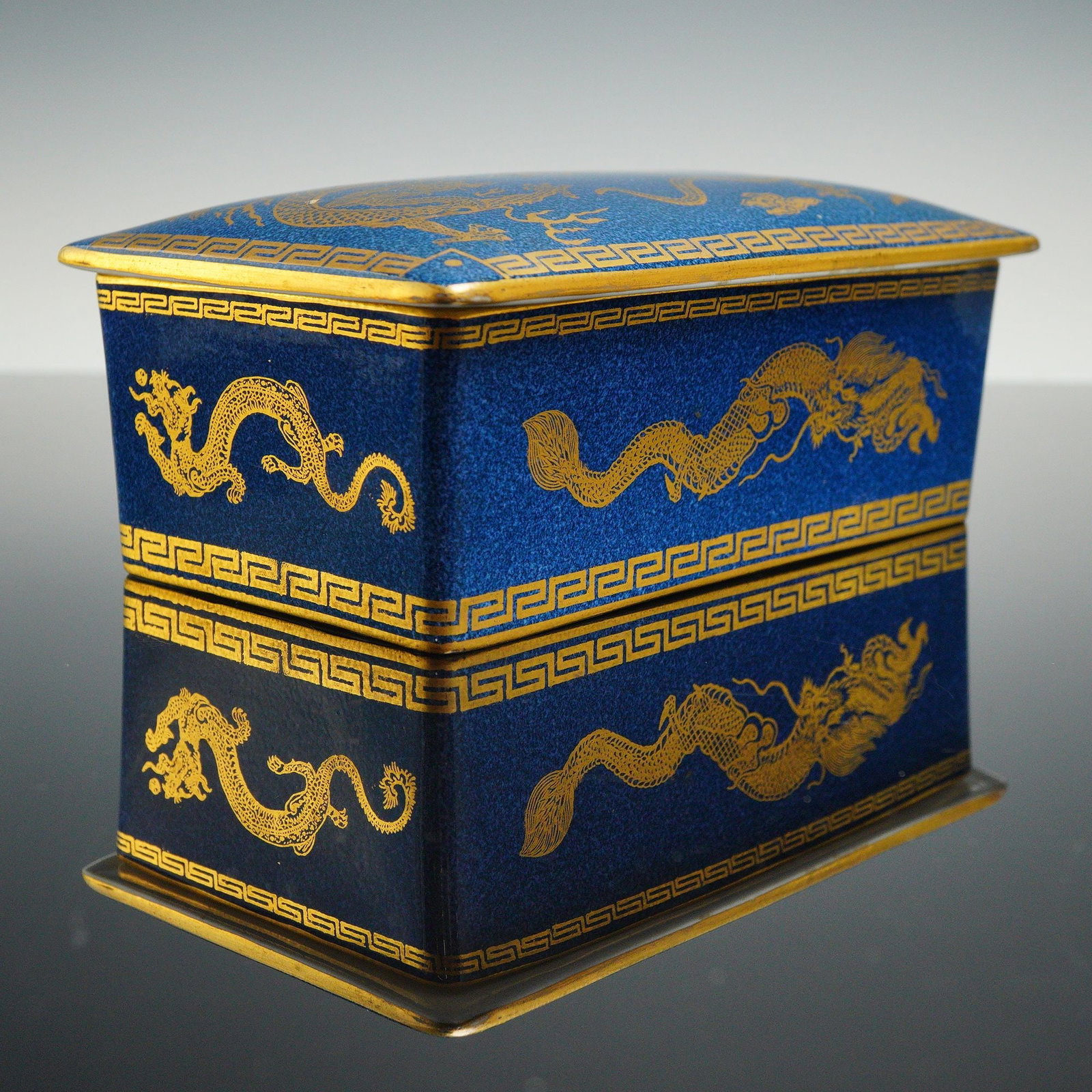 Wedgwood Bleu Souffle Lustre Dragon Lidded Box, Z4616: The lidded box features a powder-blue glazed exterior decorated with gilded dragons surrounding a Sacred Pearl. The rim and lid edges are finished with a Greek key border. The interior is porcelain wh