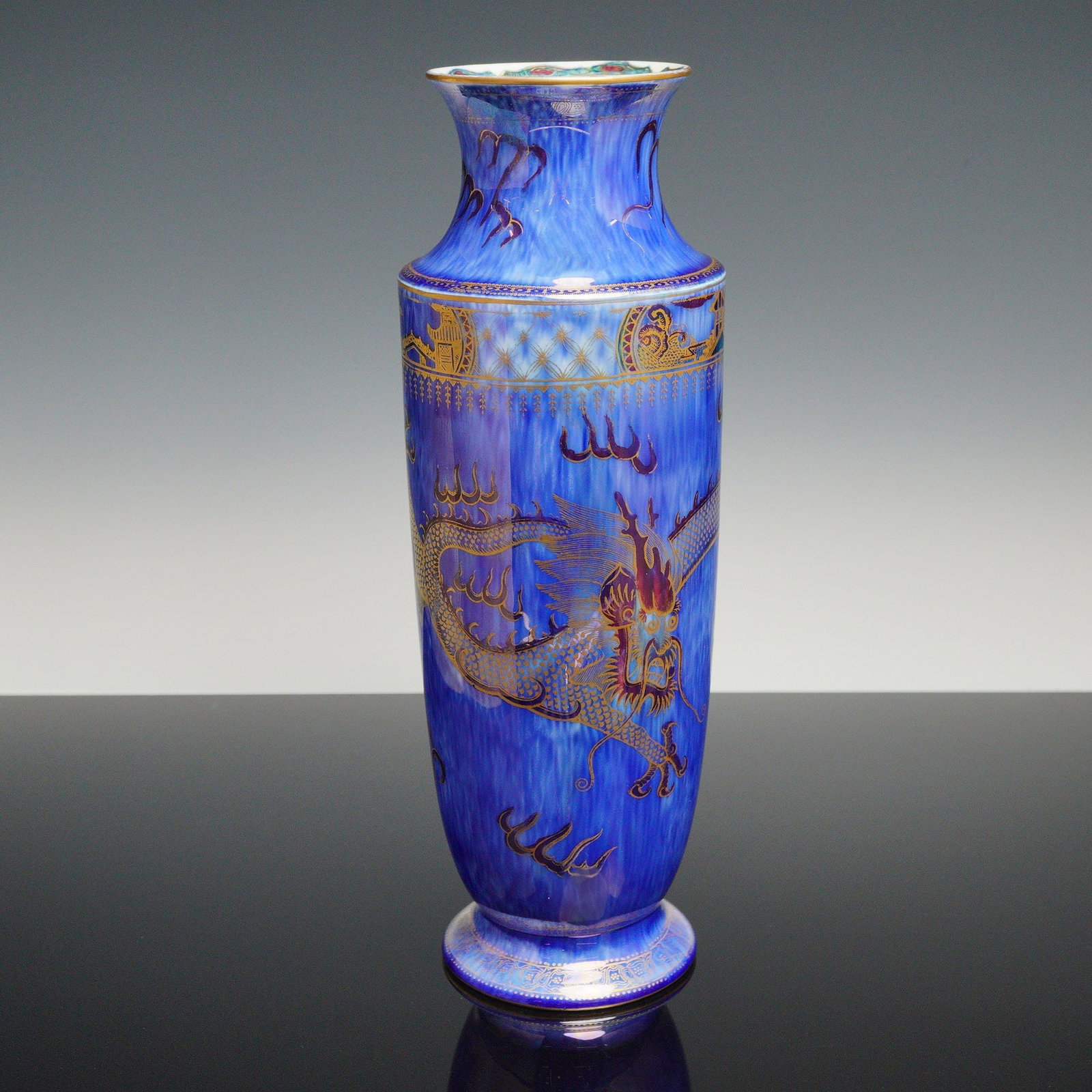 Wedgwood Fairyland Lustre Vase, Celestial Dragon Z4829: Designed by Daisy Makeig-Jones. The vase features a mottled mixed-blue exterior luster glaze with a gilt transfer-printed Celestial Dragon and stylized Sacred Pearl flames. The base and top rim have a