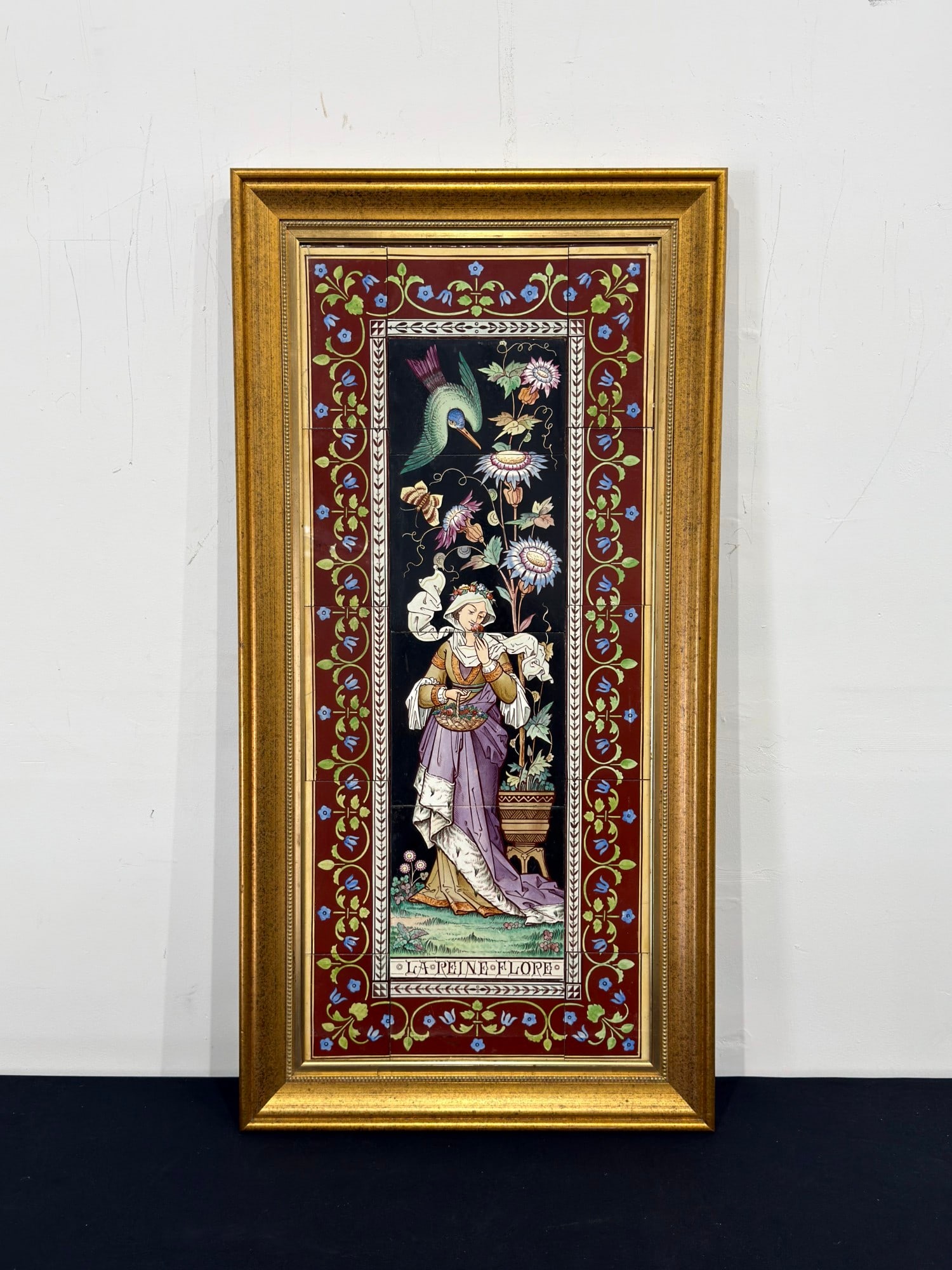 Antique Framed Minton & Co. Tile Wall Tile Panel, La Reine Flore: Late 19th century 16-tile panel housed in a gilt wood frame. The central scene depicts a woman in stylized medieval attire wearing a lavender gown with ermine-style trim and a floral crown, holding a