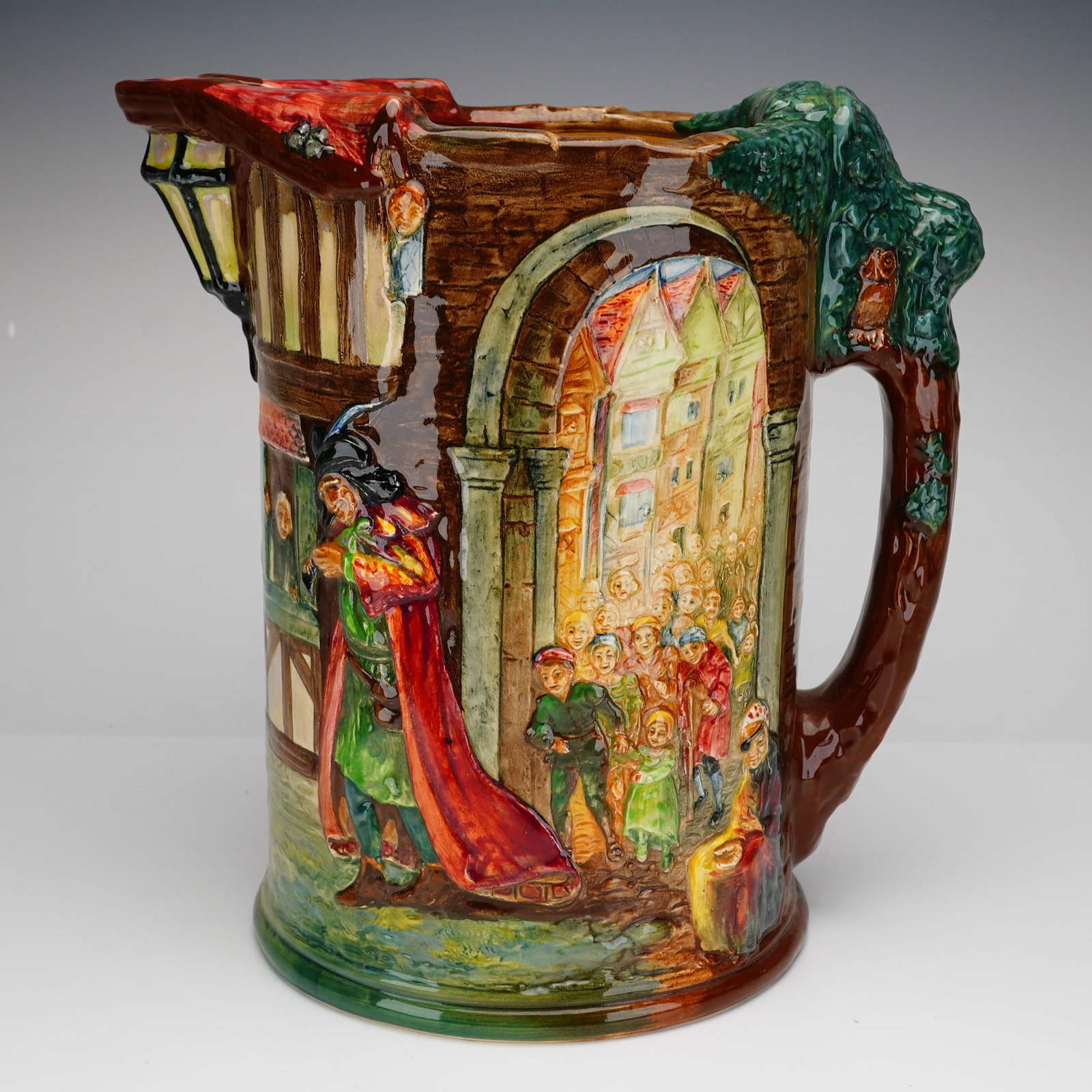 Royal Doulton Presentation Jug, The Pied Piper: This piece features a high-relief polychrome design with a glossy glaze finish. The body depicts scenes from the folk tale, including the Piper in a red cloak leading a procession of children through