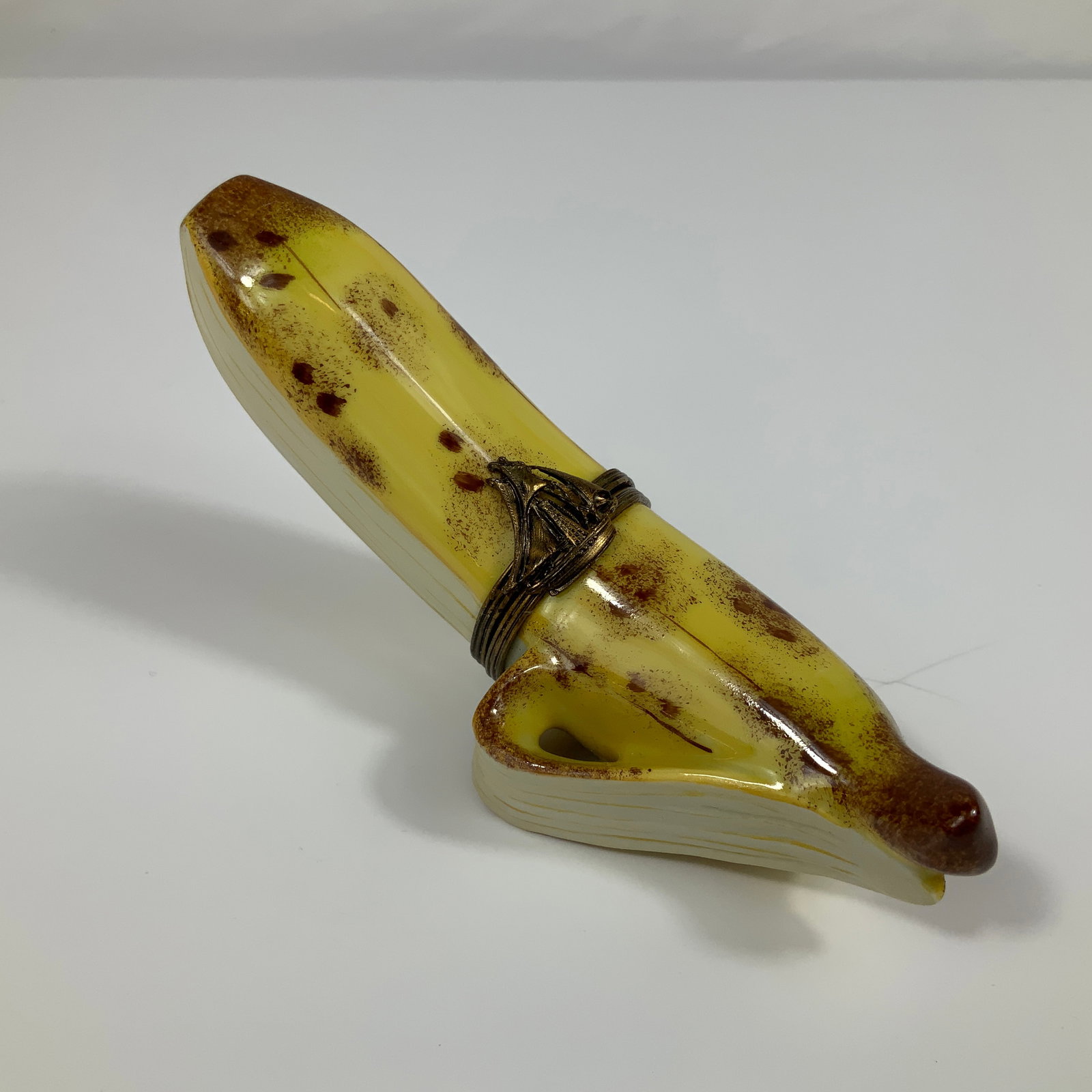 Limoges Porcelain Peeled Banana Trinket Box: This hand-painted porcelain trinket box is naturalistically modeled in the form of a partially peeled, ripening banana. The exterior is finished with a yellow glaze accented by brown stippling and spo