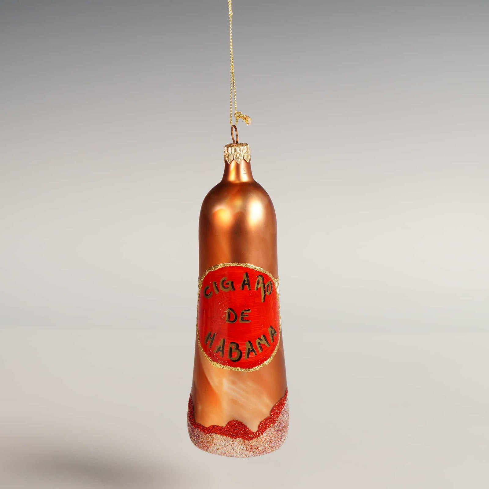 Glass Cigaro De Habana Christmas Ornament: Mouth-blown glass ornament shaped as a cigar with metallic copper finish, red and white decorative banding, and glittered base. The piece is inscribed "Cigaro de Habana," a stylized phrase inspired by