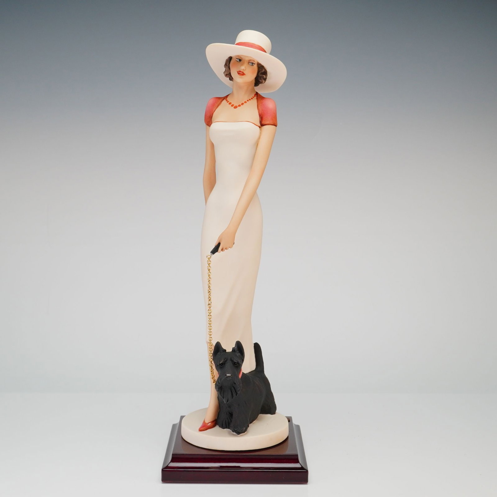 Florence Giuseppe Armani Figurine Edith 2237C: The figure depicts a woman in Art Deco style attire, featuring a wide-brimmed white hat with a red ribbon, a red bolero-style shrug, and a long white sleeveless gown. She is shown walking a black Scot
