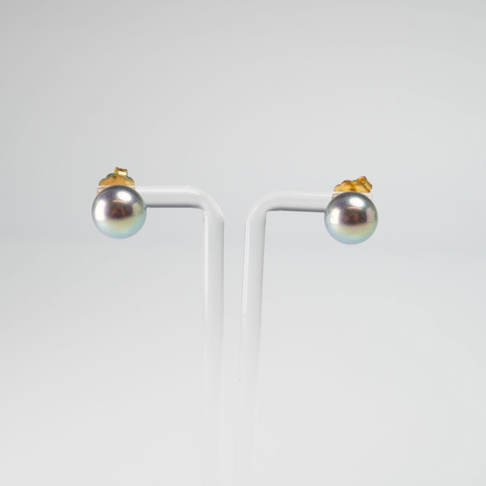 Pair of 1/20 14K Gold Filled and Cultured Pearl Stud Earrings: This matched pair of stud earrings features two round cultured pearls. The pearls exhibit a dark body color with a metallic peacock iridescent luster. The earrings are constructed with gold-toned meta