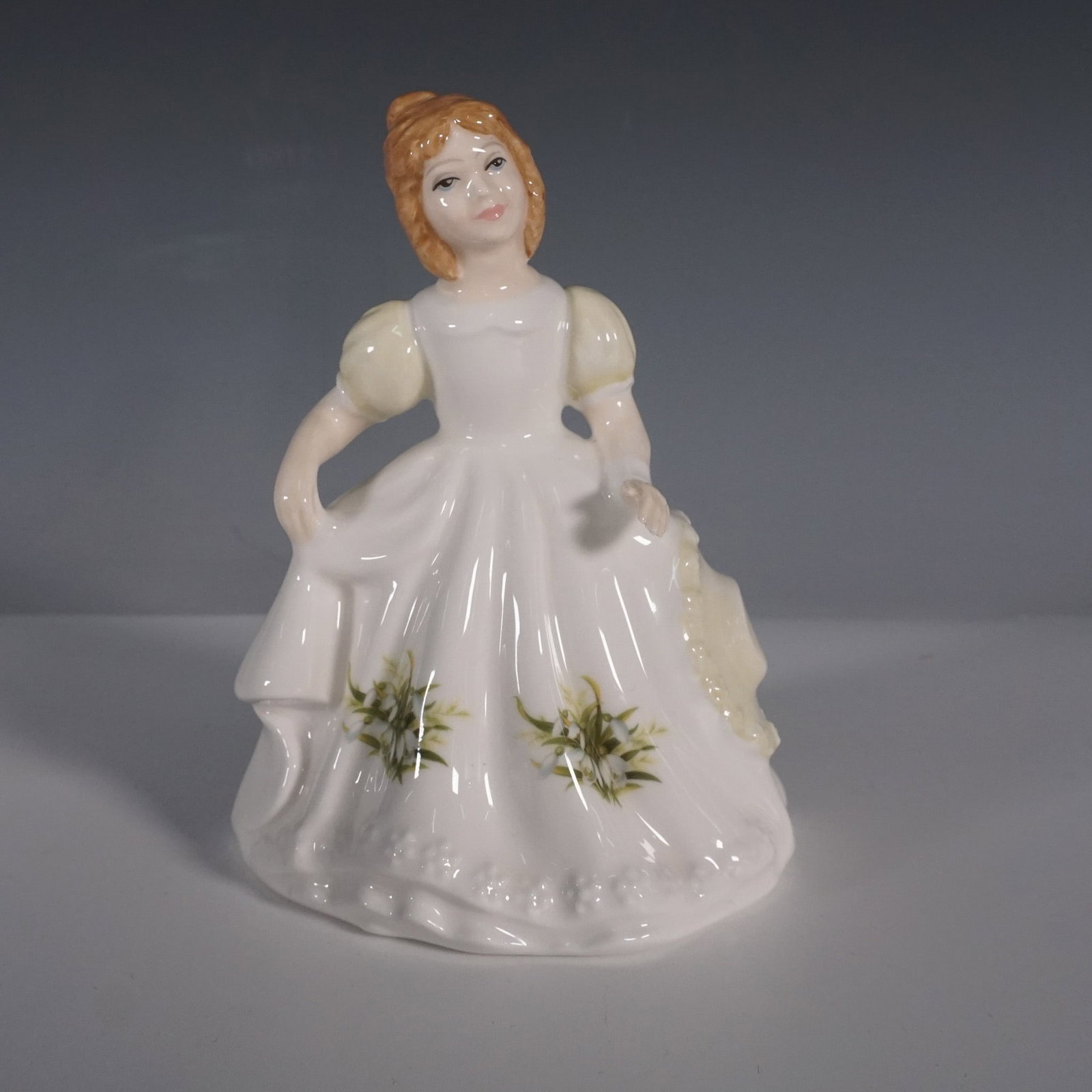 Royal Doulton Figurine January HN3328: Royal Doulton porcelain figurine titled January, model HN3328, from the Figure of the Month series. This charming piece features a young girl in a flowing white dress adorned with delicate floral acce