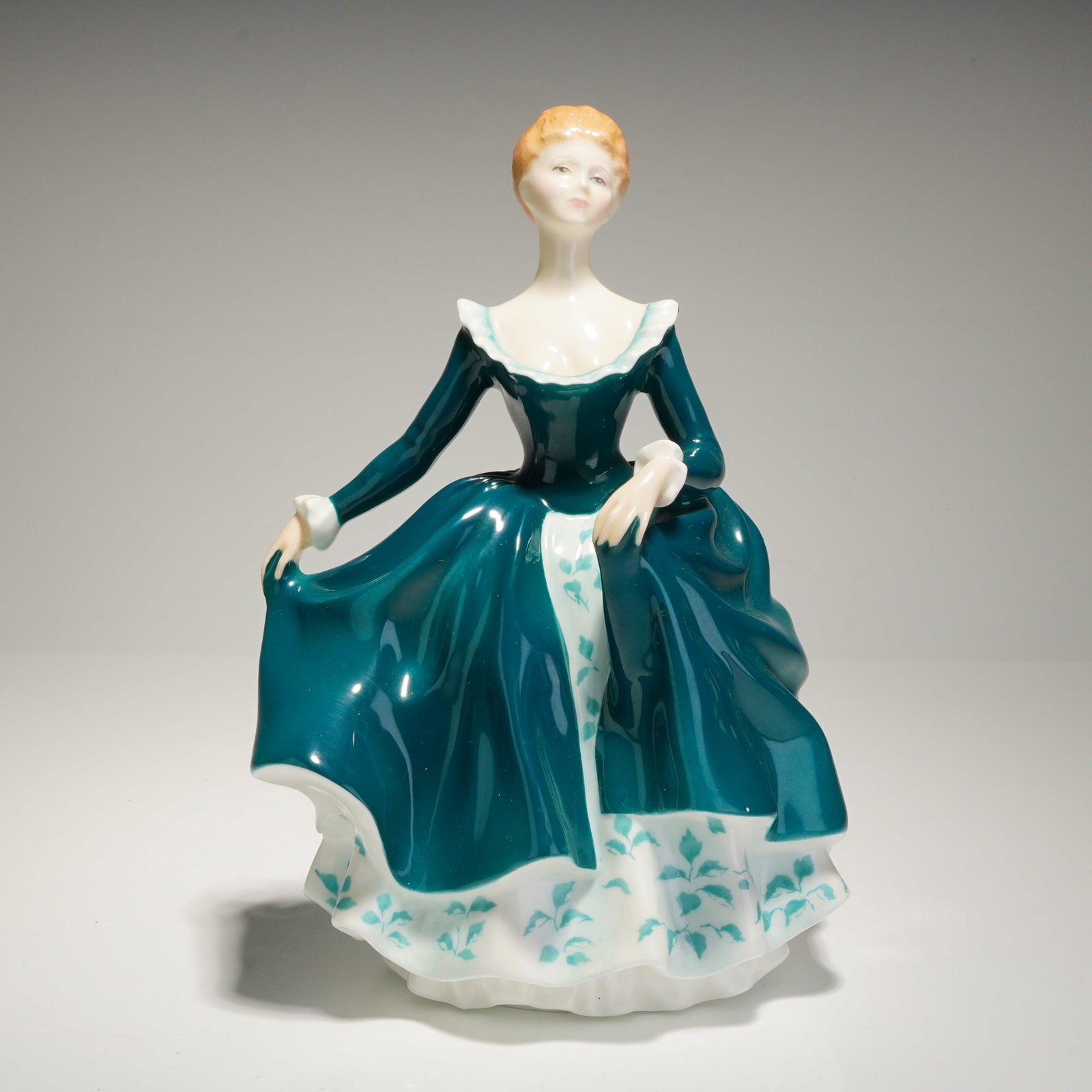 Royal Doulton Porcelain Figurine Janine HN2461: A single Royal Doulton porcelain figurine titled 'Janine,' model number HN 2461. The figure depicts a standing woman with auburn hair, dressed in a voluminous, highly glossy gown of deep teal. The dre