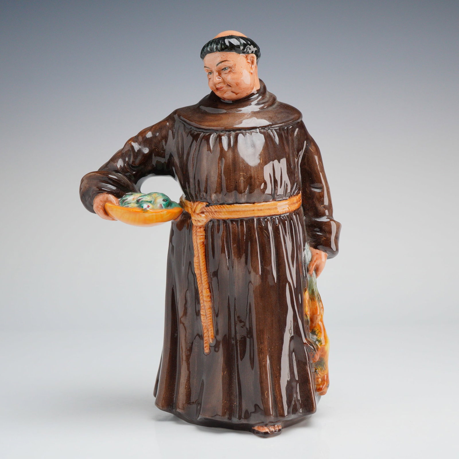Royal Doulton Figurine, Jovial Monk HN2144: A Royal Doulton glazed ceramic figurine titled The Jovial Monk, model number HN 2144. The figure is depicted in a traditional brown habit with a yellow cord belt, carrying a shallow bowl of fish in hi