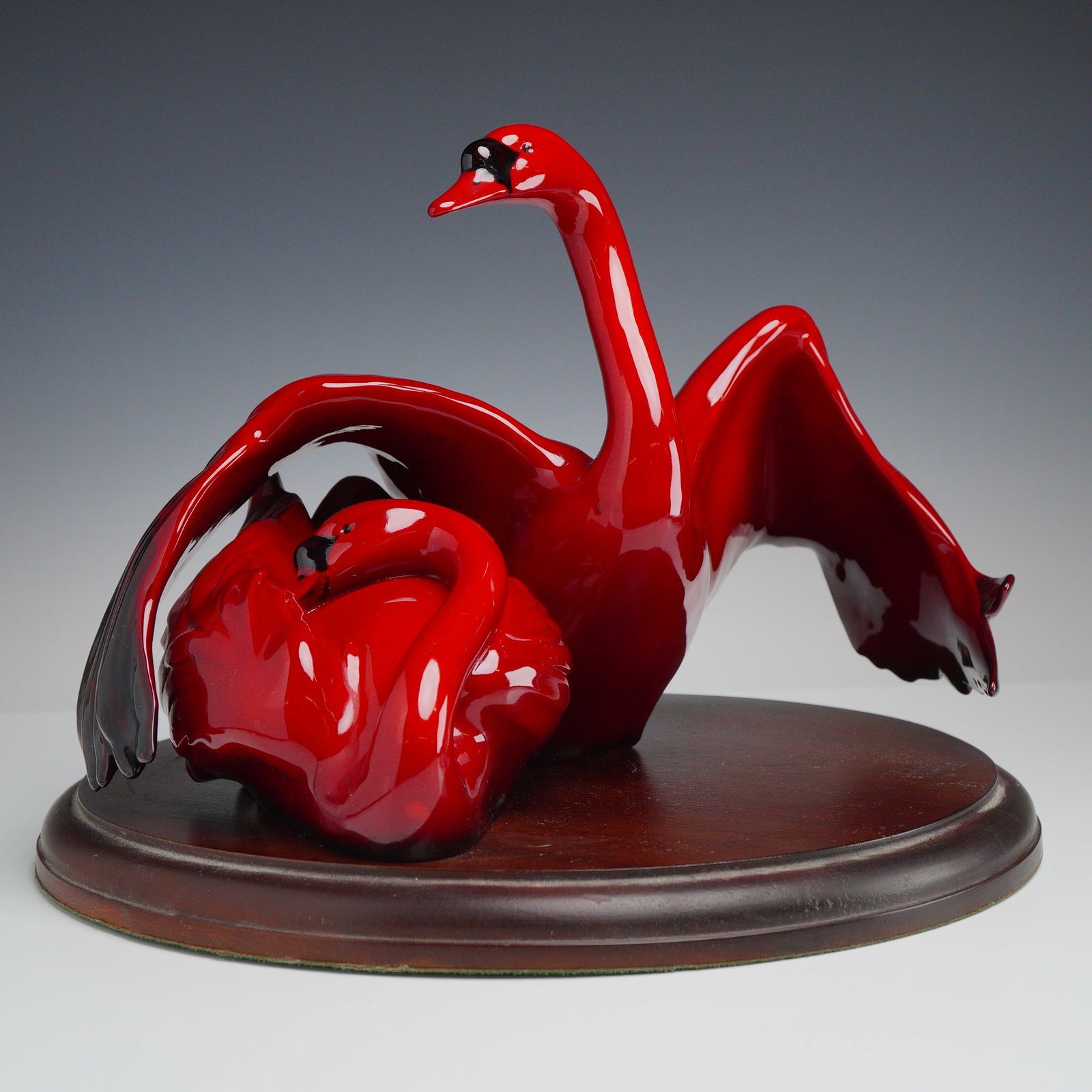 Royal Doulton Flambe Images of Fire Figurine, Nestling Down HN3538 with Base: This handmade sculpture depicts two stylized swans, with one bird standing with its wings unfurled and the second bird nestled at the base. The piece is finished in a vibrant, high-gloss red glaze wit