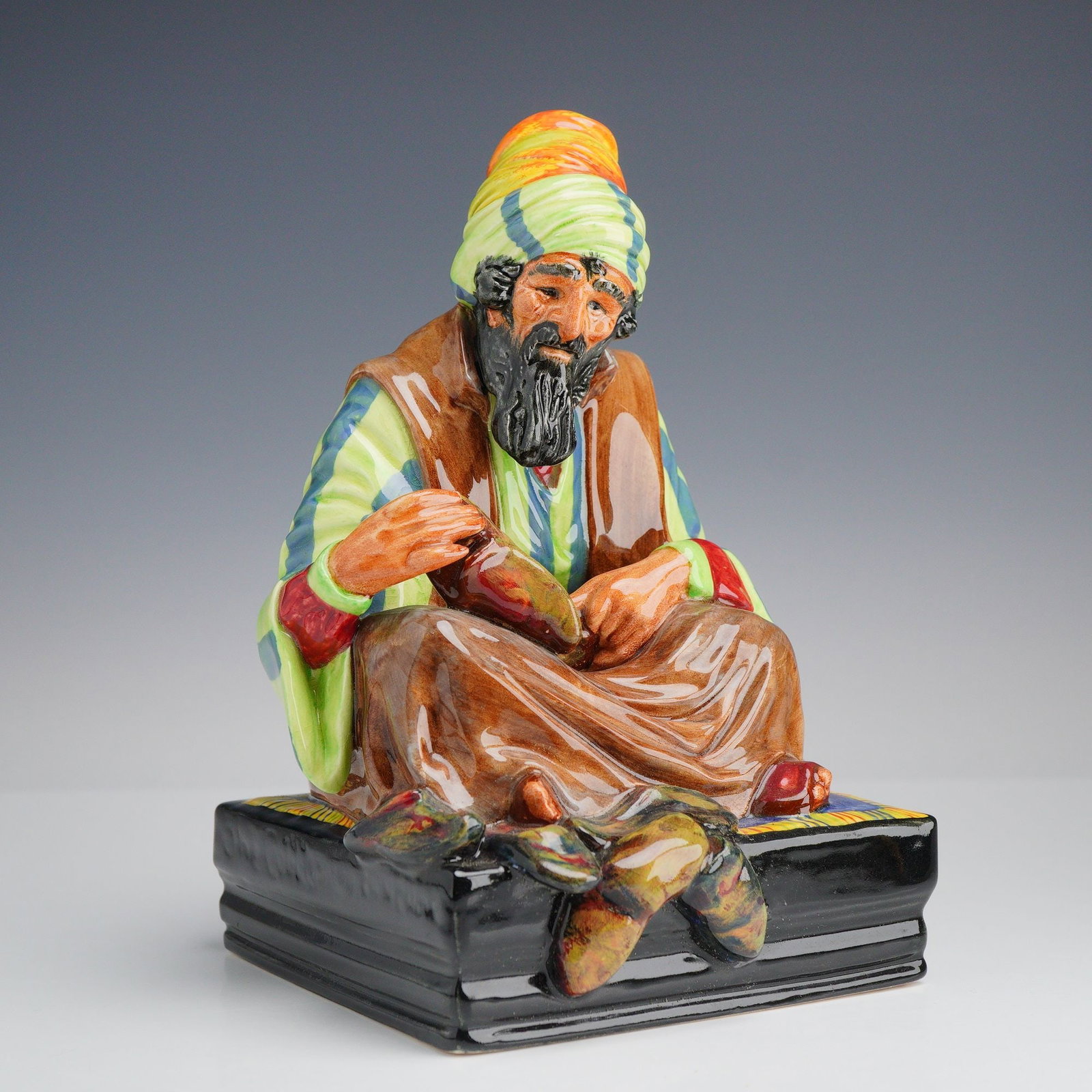 Royal Doulton Glazed Ceramic Figurine The Cobbler HN 1706: This Royal Doulton glazed ceramic figurine is titled The Cobbler, model number HN 1706. The figure depicts a man with a dark beard and mustache wearing a multi-colored turban in shades of orange, yell