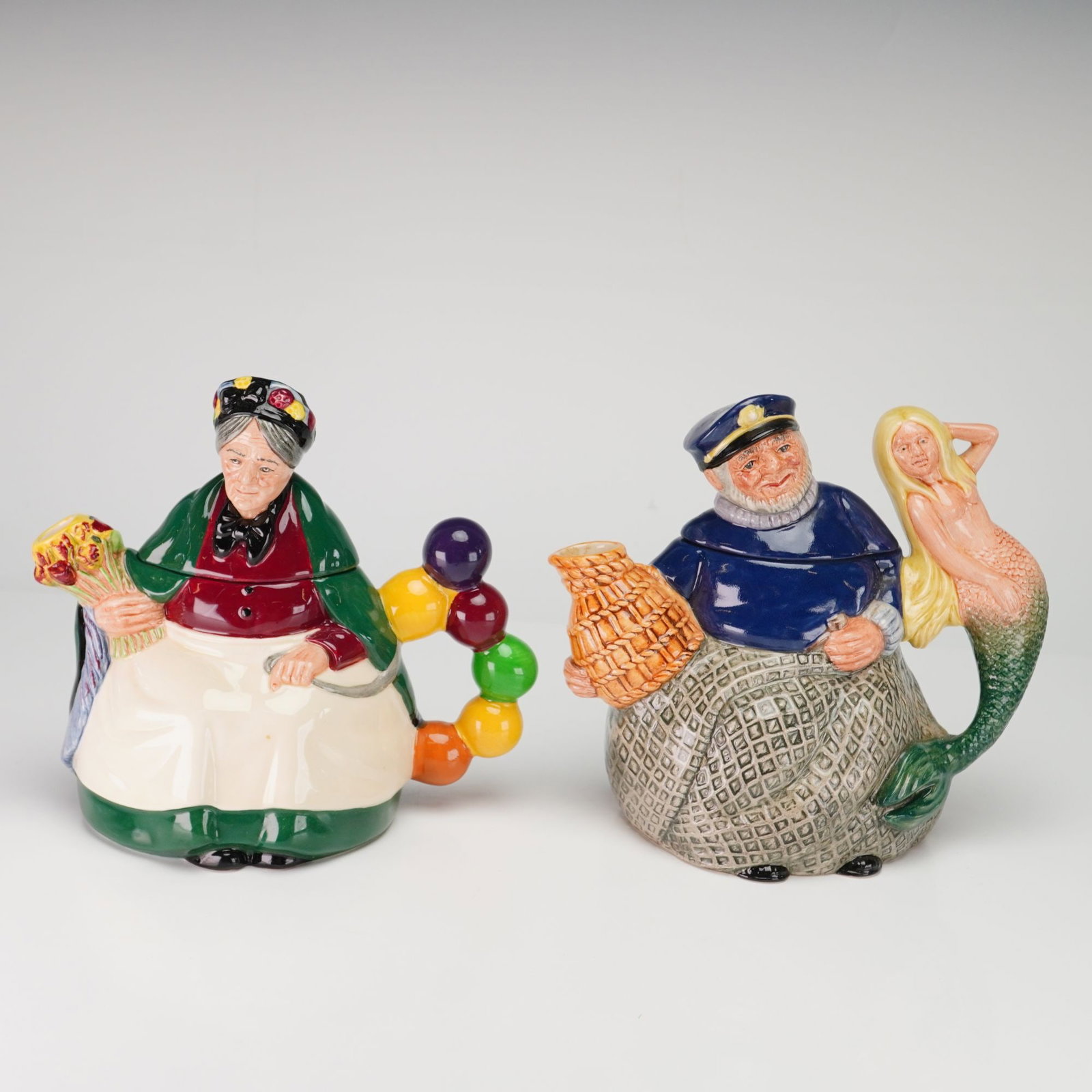 A Pair of Royal Doulton Figurine Character Teapots, Old Balloon Seller and Old Salt: This lot comprises two Royal Doulton figurine character teapots, both modeled by William K. Harper. The Old Balloon Seller (D 6855) features a woman in a green cloak and white apron with a bouquet-for