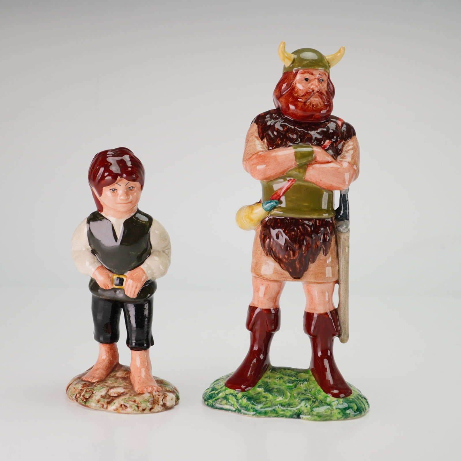 Two Royal Doulton Middle Earth Figurines, Frodo HN 2912 and Boromir HN2918: This pair of glazed ceramic figurines belongs to the Royal Doulton Middle Earth collection, produced under license from Tolkien Enterprises. The set comprises the characters Frodo and Boromir, featuri