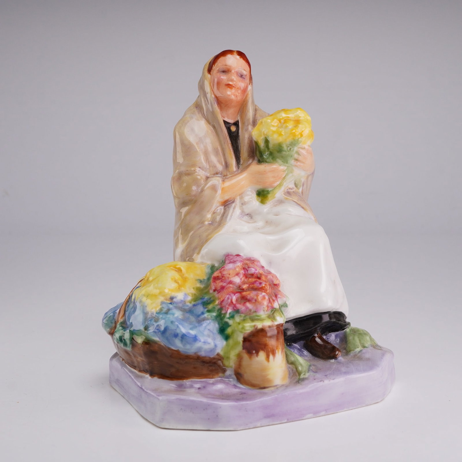 Royal Worcester Figurine, Dublin Flower Girl 2921: A Royal Worcester glazed porcelain figurine titled Dublin Flower Girl, model number 2921. The piece was modeled by artist Anne Acheson. The figure depicts a seated woman dressed in a tan shawl and whi