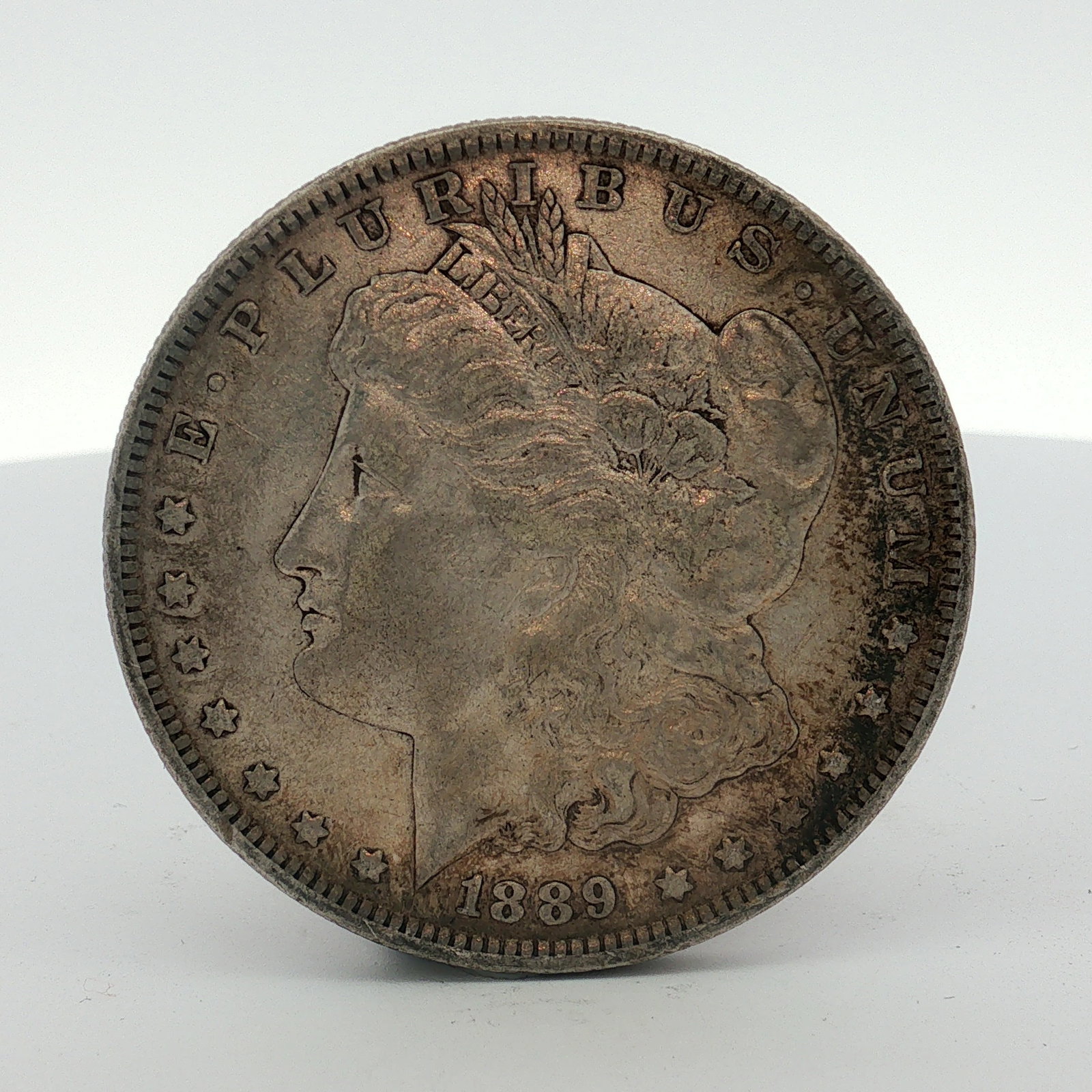 1889-O US Morgan Silver Dollar: This US Morgan silver dollar was struck at the New Orleans Mint in 1889. The coin features a reeded edge and is made of 90% silver and 10% copper. The obverse displays the Morgan dollar design with th