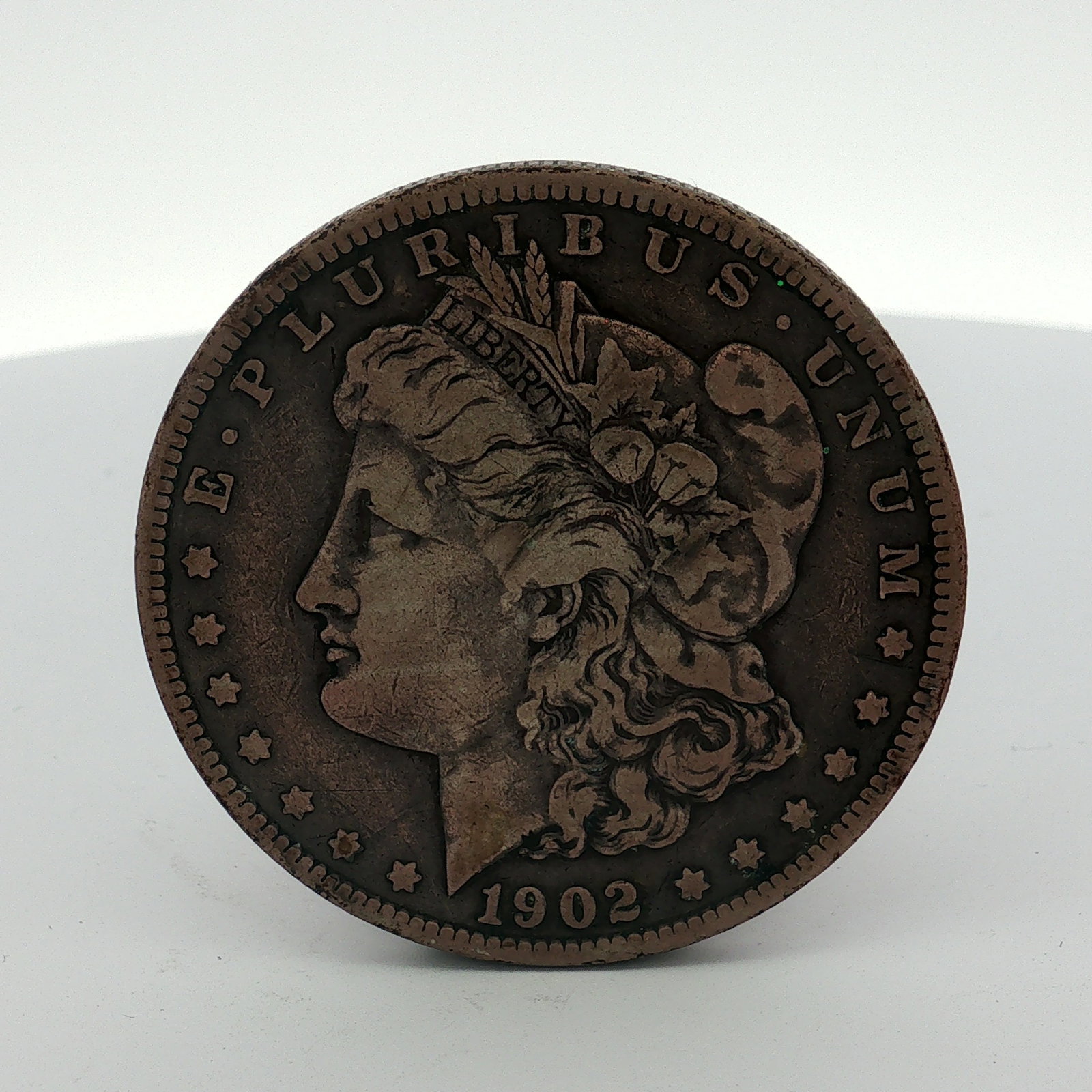 1902 US One Dollar Morgan Silver Dollar, Circulated: 1902 US Morgan dollar is a Philadelphia mint issue, identified by the absence of a mint mark. The piece features the standard Morgan dollar design and a reeded edge. The composition appears to be a ba